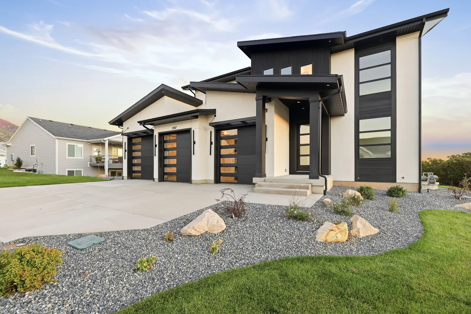 Front exterior with dark trim, two garage doors, concrete driveway, and landscaped front yard at sunset in Hawthorne Modern, Ogden.