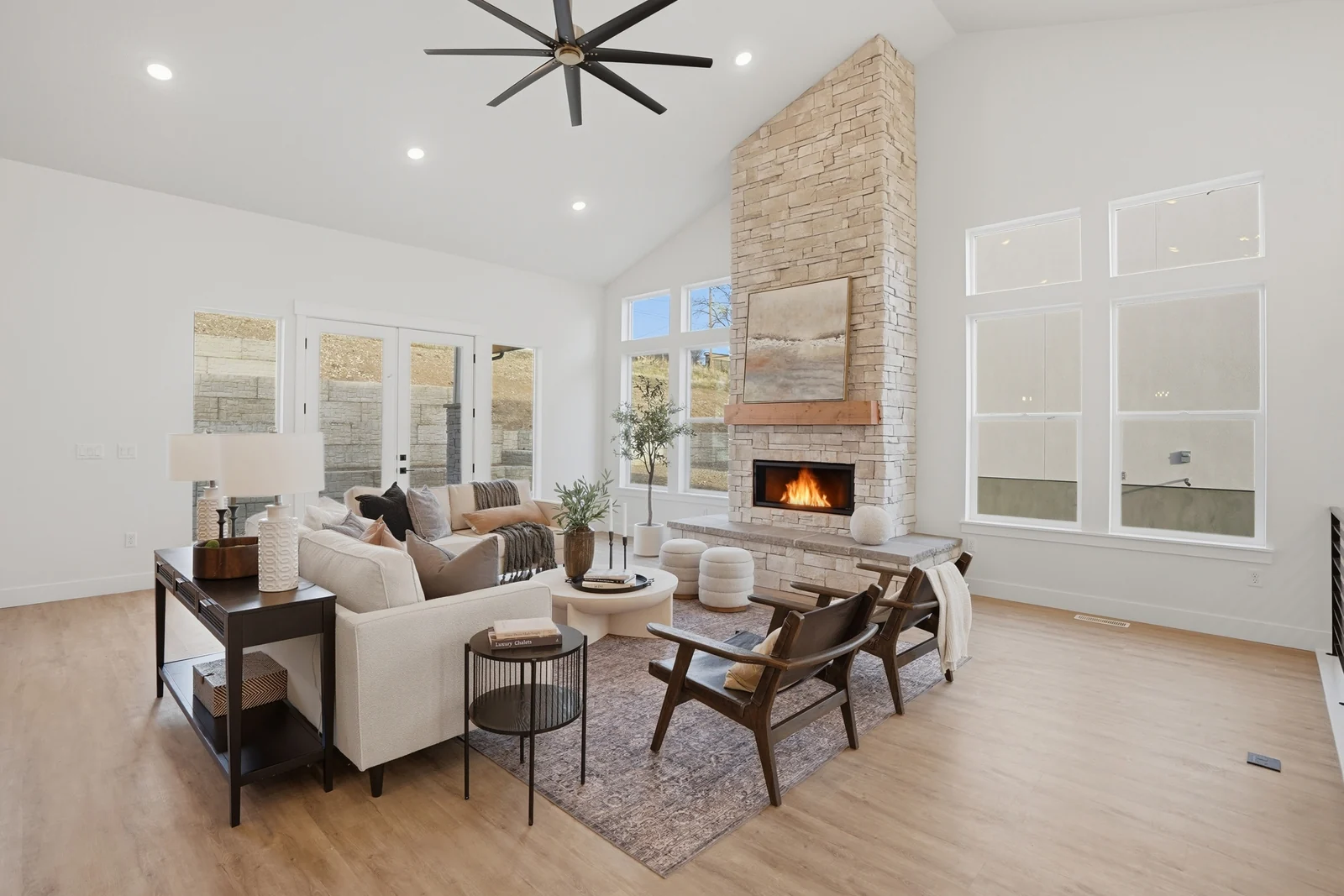 Great room with stone fireplace, white seating, wood flooring, and a wall of windows in Olympic BH08, American Fork.