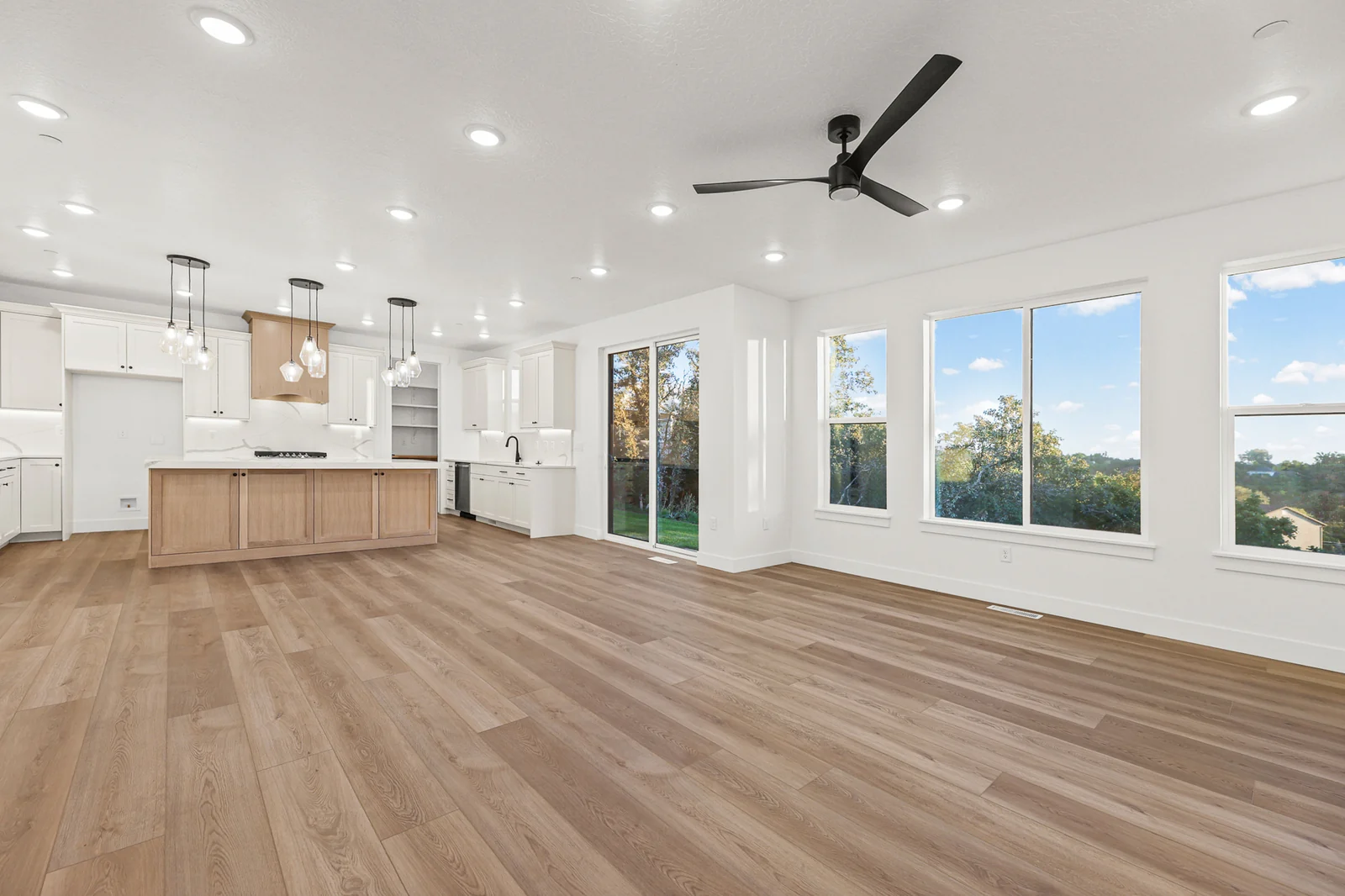 Open great room with wood-look flooring, ceiling fan, large windows, kitchen island, and pendant lights in Hawthorne Modern, Ogden.