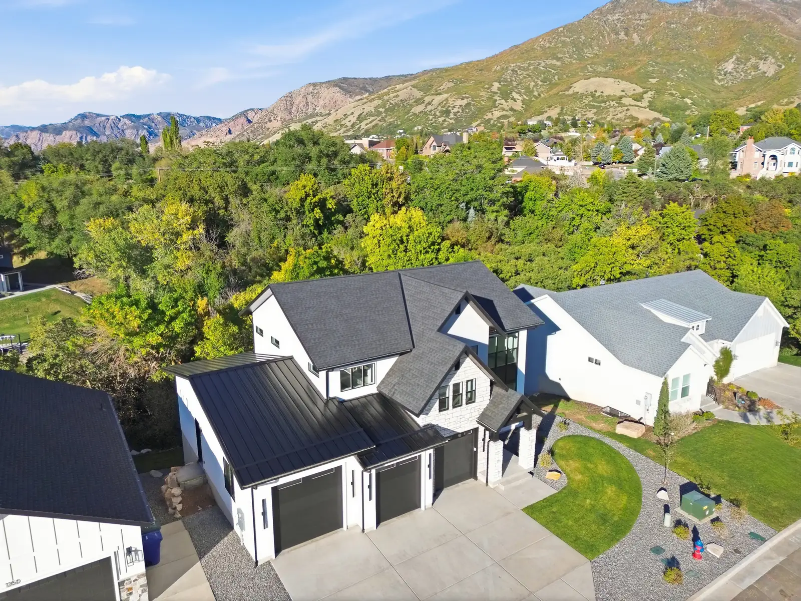 Aerial photo shows the home near wooded terrain, neighboring roofs, and mountains beyond in Hawthorne Farmhouse, Ogden.