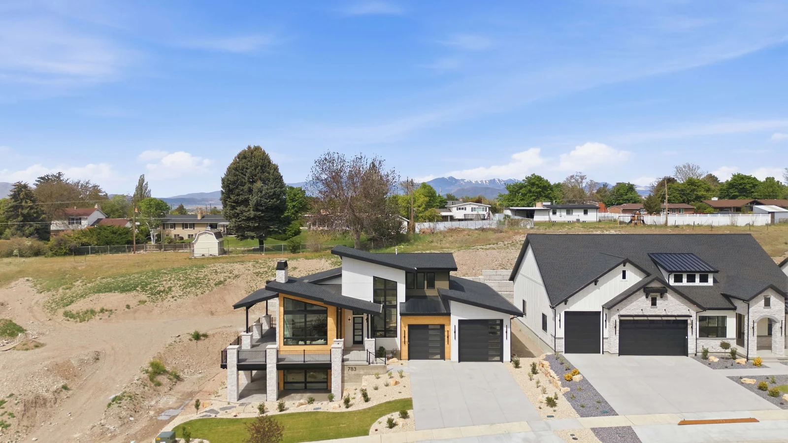 Aerial view of the house within its neighborhood, showing the driveway, adjacent construction areas, homes, and distant hills in the Denali model, American Fork.