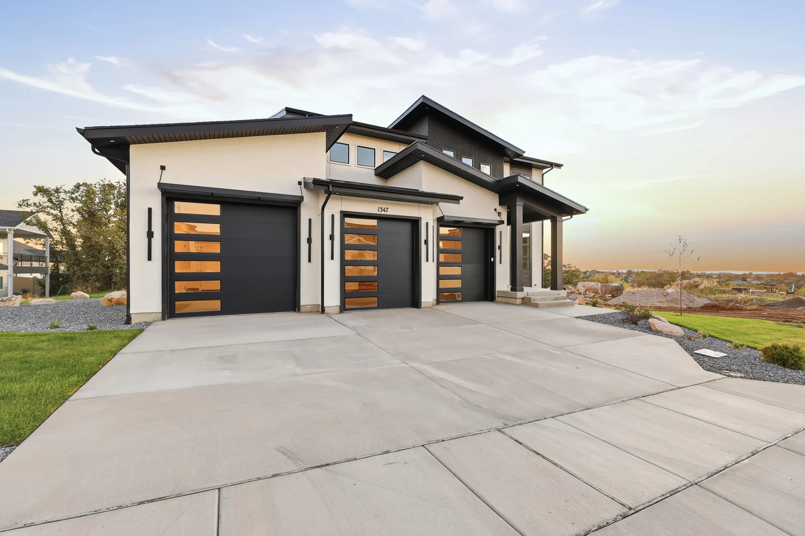 Front exterior with concrete driveway, two garage doors, dark trim, and mountain view at sunset in Hawthorne Modern, Ogden.