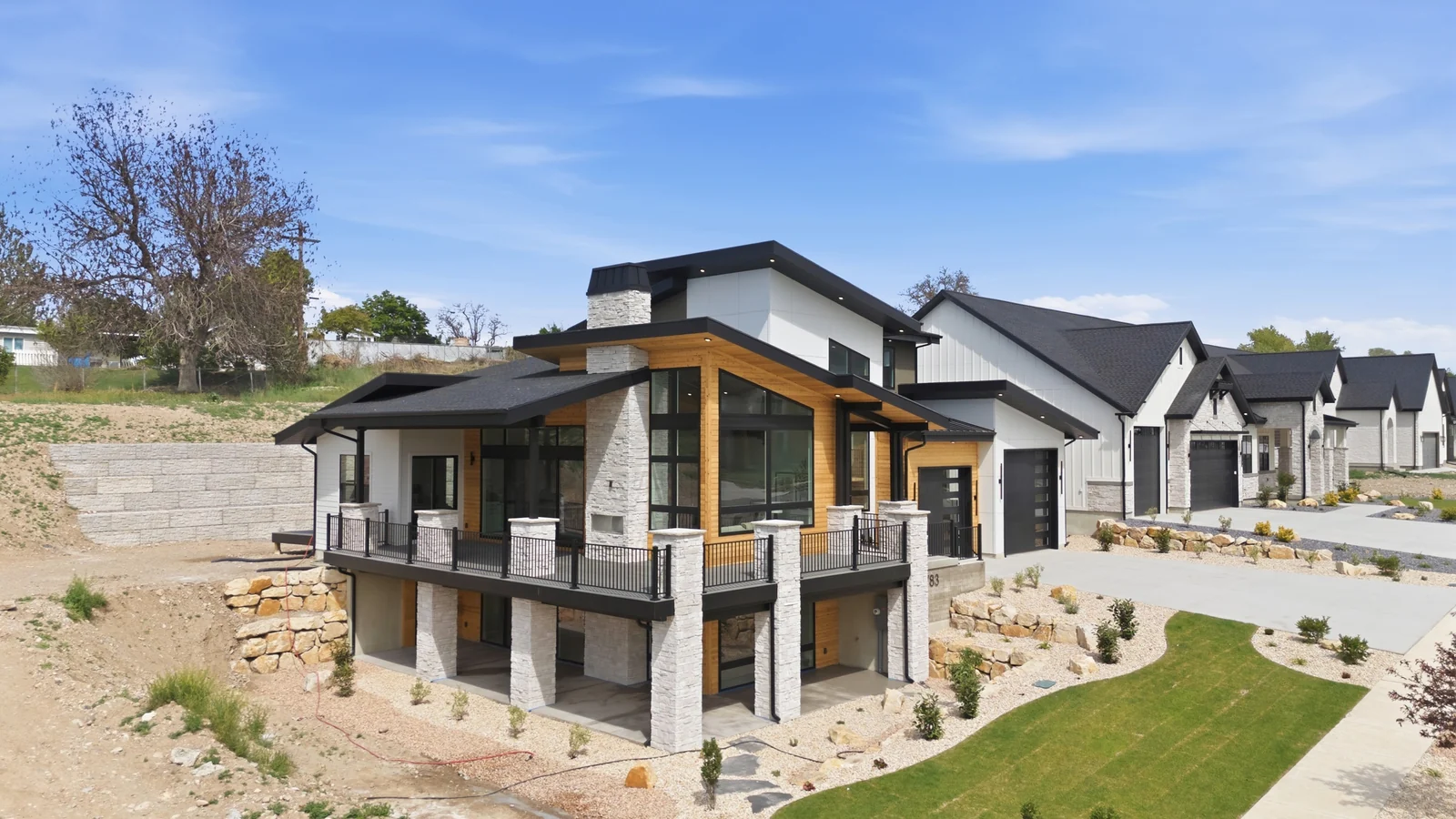 Aerial rear-quarter view showing the two-story exterior, covered deck, lawn, driveway, and neighboring homes in the Denali model, American Fork.
