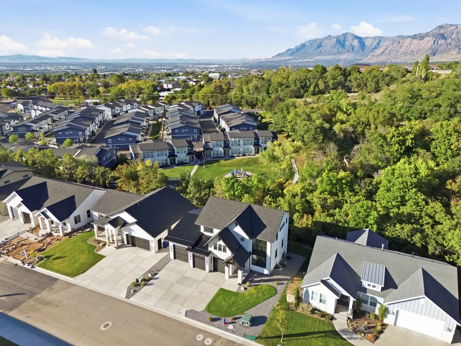 Aerial photo centers the home within a neighborhood, with tree cover and distant mountain scenery in Hawthorne Farmhouse, Ogden.