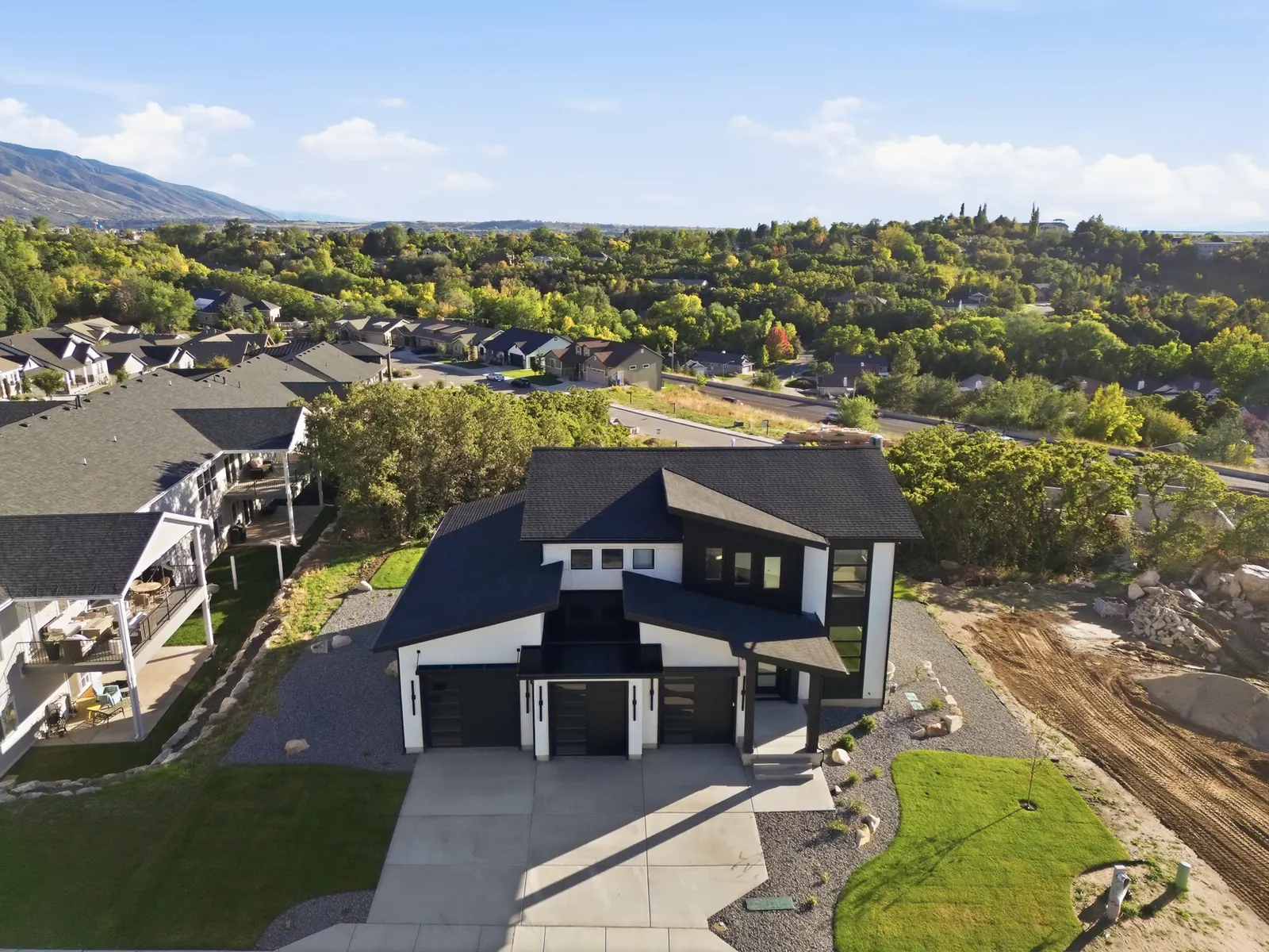 Aerial photograph showing the home, nearby neighborhood, wooded hillside, streets, and distant mountain terrain in Hawthorne Modern, Ogden.