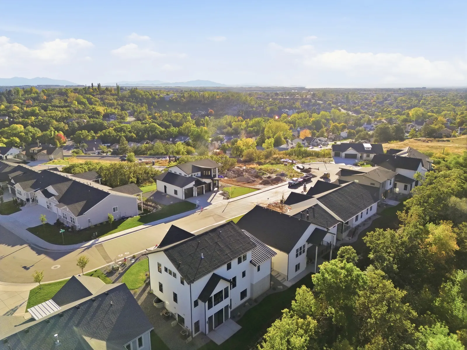 Elevated aerial view shows nearby homes, streets, dense trees, and mountain slopes in Hawthorne Farmhouse, Ogden.
