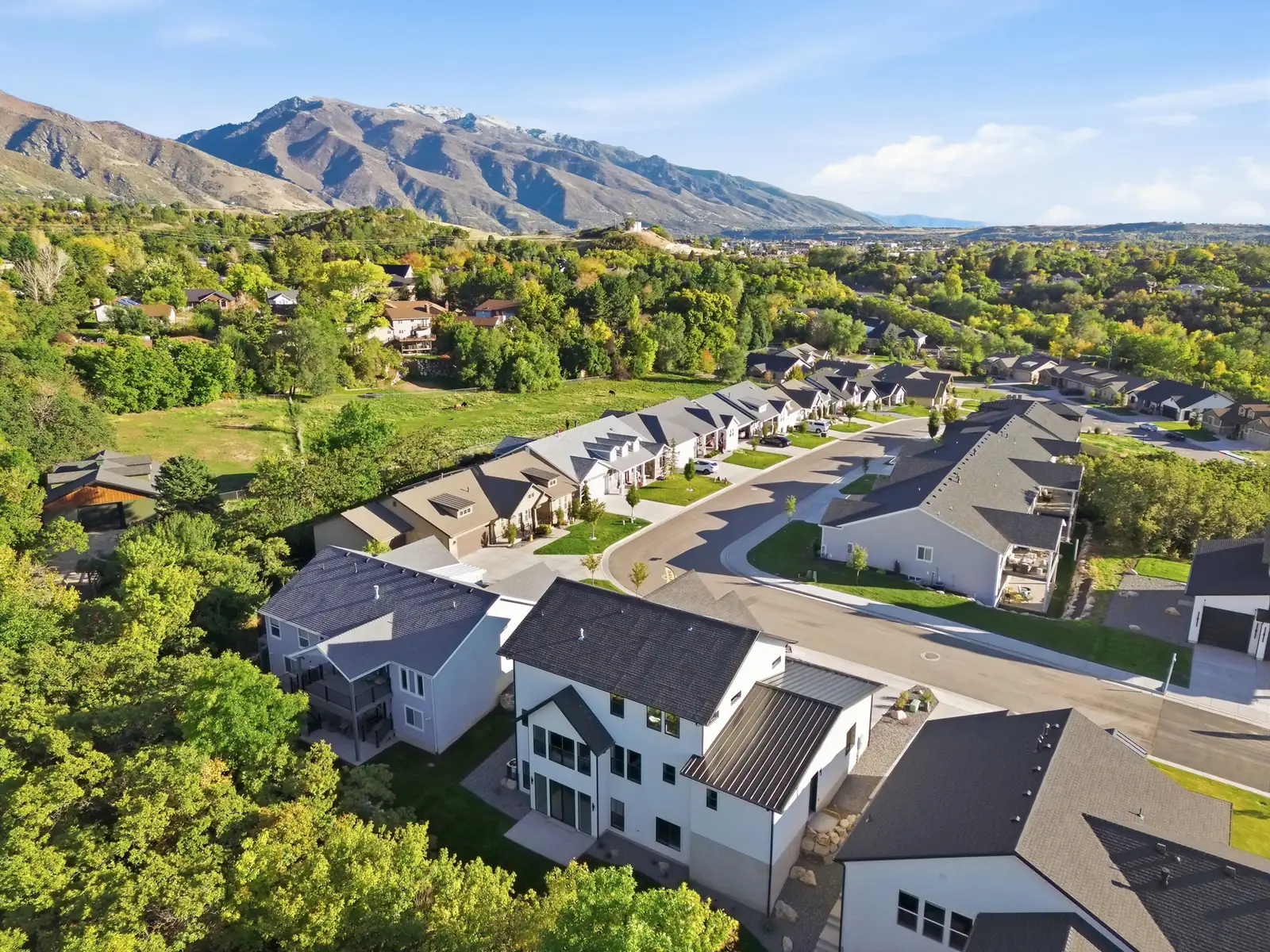 Aerial view looks across surrounding roofs, mature trees, broad valley, and mountains in Hawthorne Farmhouse, Ogden.