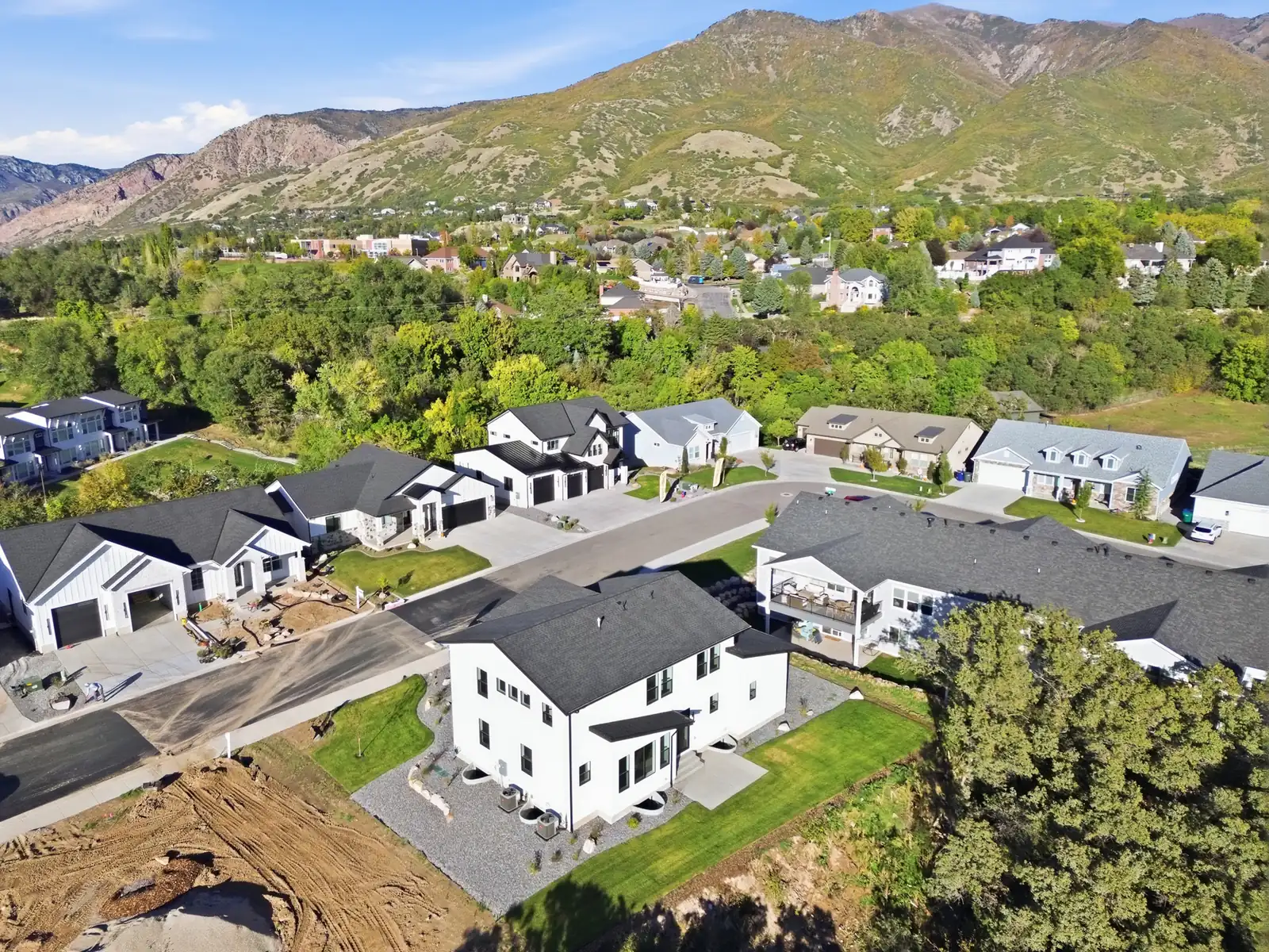 Aerial photograph showing the rear of the home, neighboring houses, green trees, and mountain hillside in Hawthorne Modern, Ogden.