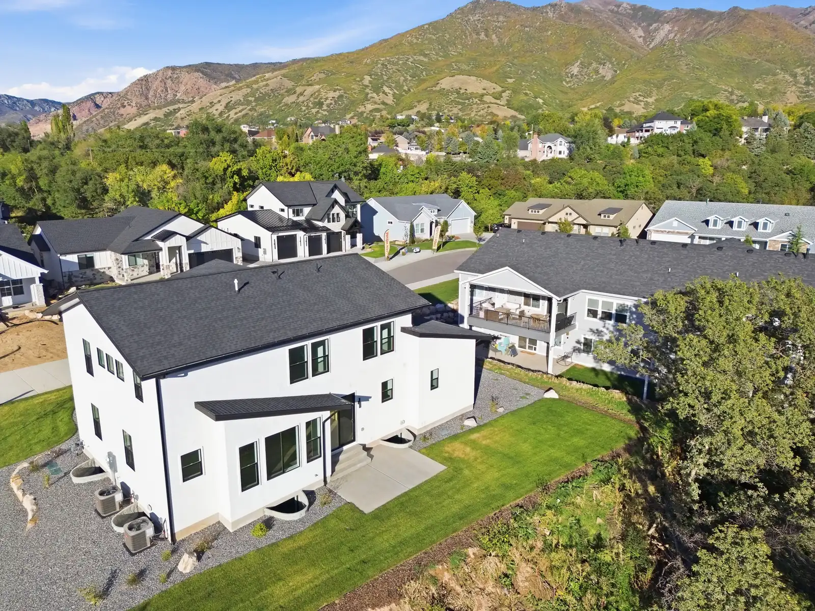 Aerial photograph of the rear exterior, lawn, surrounding homes, mature trees, and mountain hillside in Hawthorne Modern, Ogden.