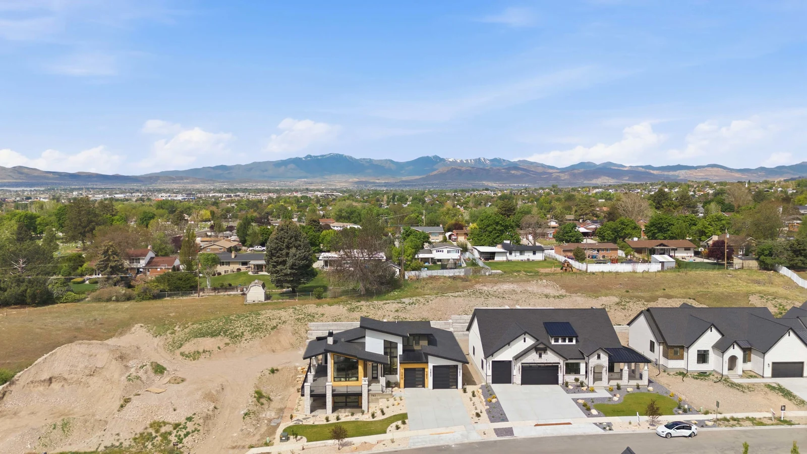 Aerial view of the home along the street, with neighboring roofs, driveways, unfinished ground, and mountain backdrop in the Denali model, American Fork.
