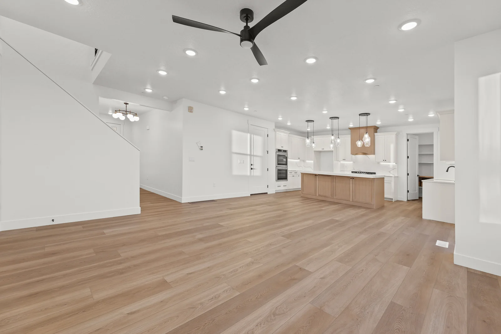 Open great room with wood-look flooring, recessed lights, kitchen cabinetry, island, and staircase in Hawthorne Modern, Ogden.