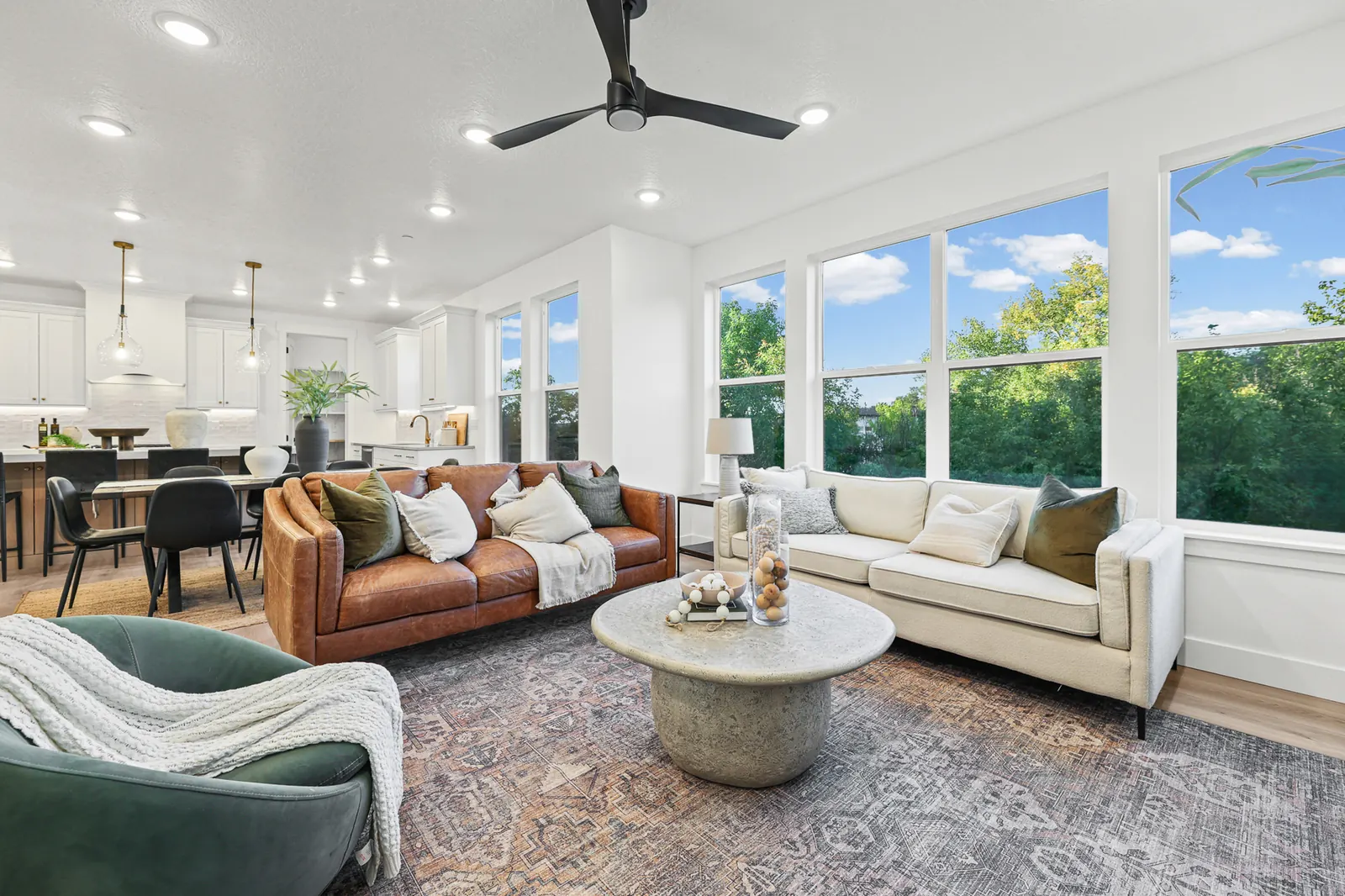 Staged living room opens toward a kitchen and dining area through expansive corner windows in Hawthorne Farmhouse, Ogden.