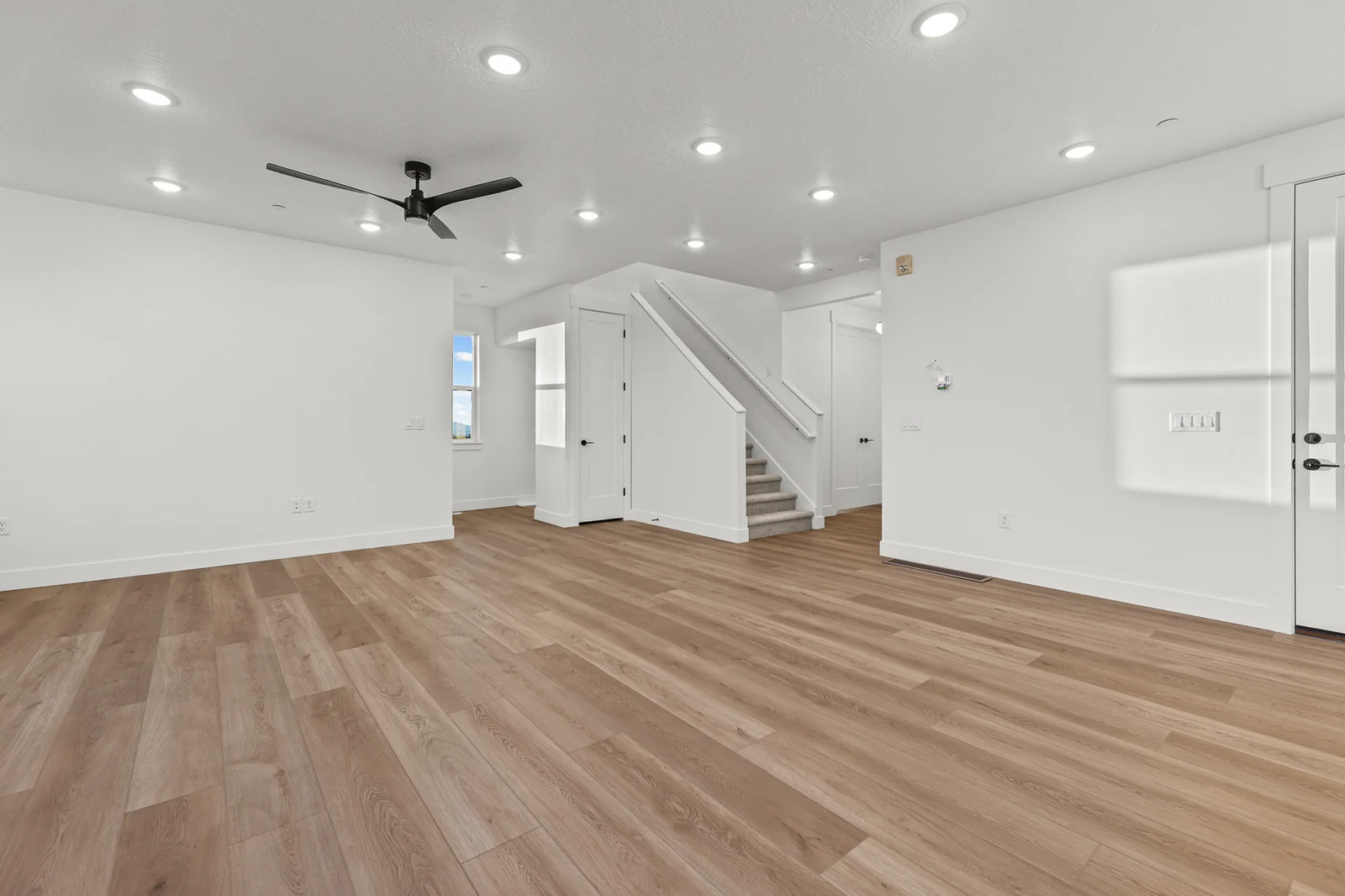 Open great room with wood-look flooring, ceiling fan, recessed lights, white stairway, and interior doorways in Hawthorne Modern, Ogden.