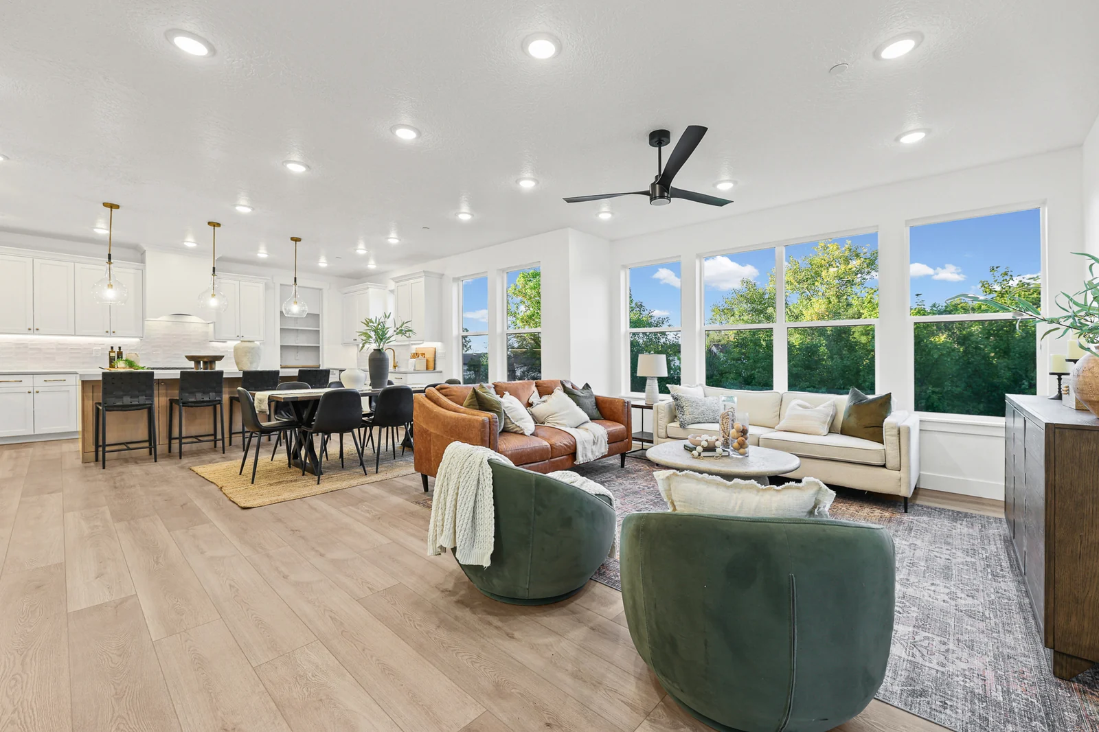 Staged great room shows seating, dining table, kitchen island, large windows, and light wood flooring in Hawthorne Farmhouse, Ogden.