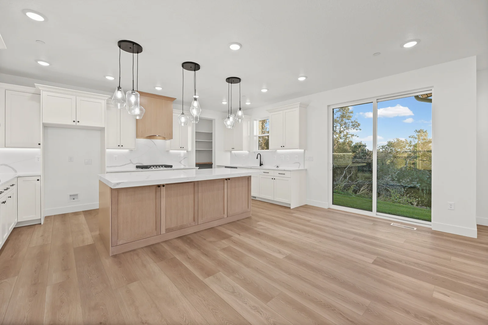 Kitchen with wood island cabinetry, white counters, pendant lights, white cabinets, and sliding glass door in Hawthorne Modern, Ogden.