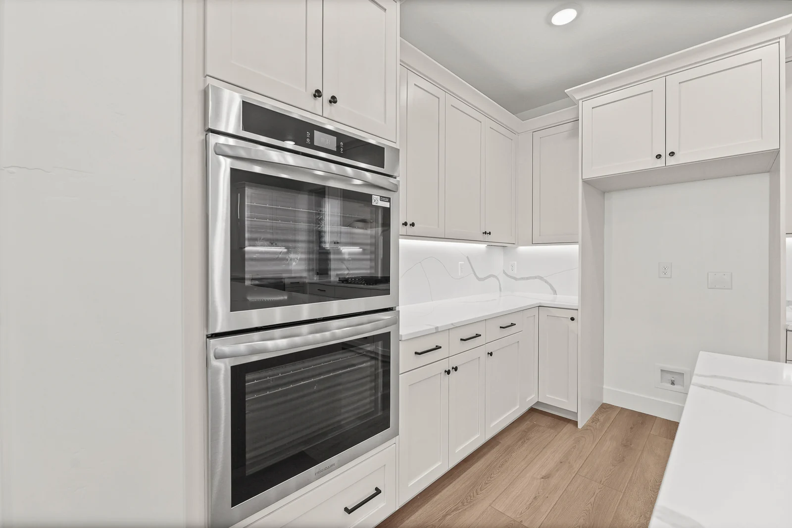 Kitchen with built-in double ovens, white cabinetry, wood-look flooring, recessed lights, and a counter edge in Hawthorne Modern, Ogden.