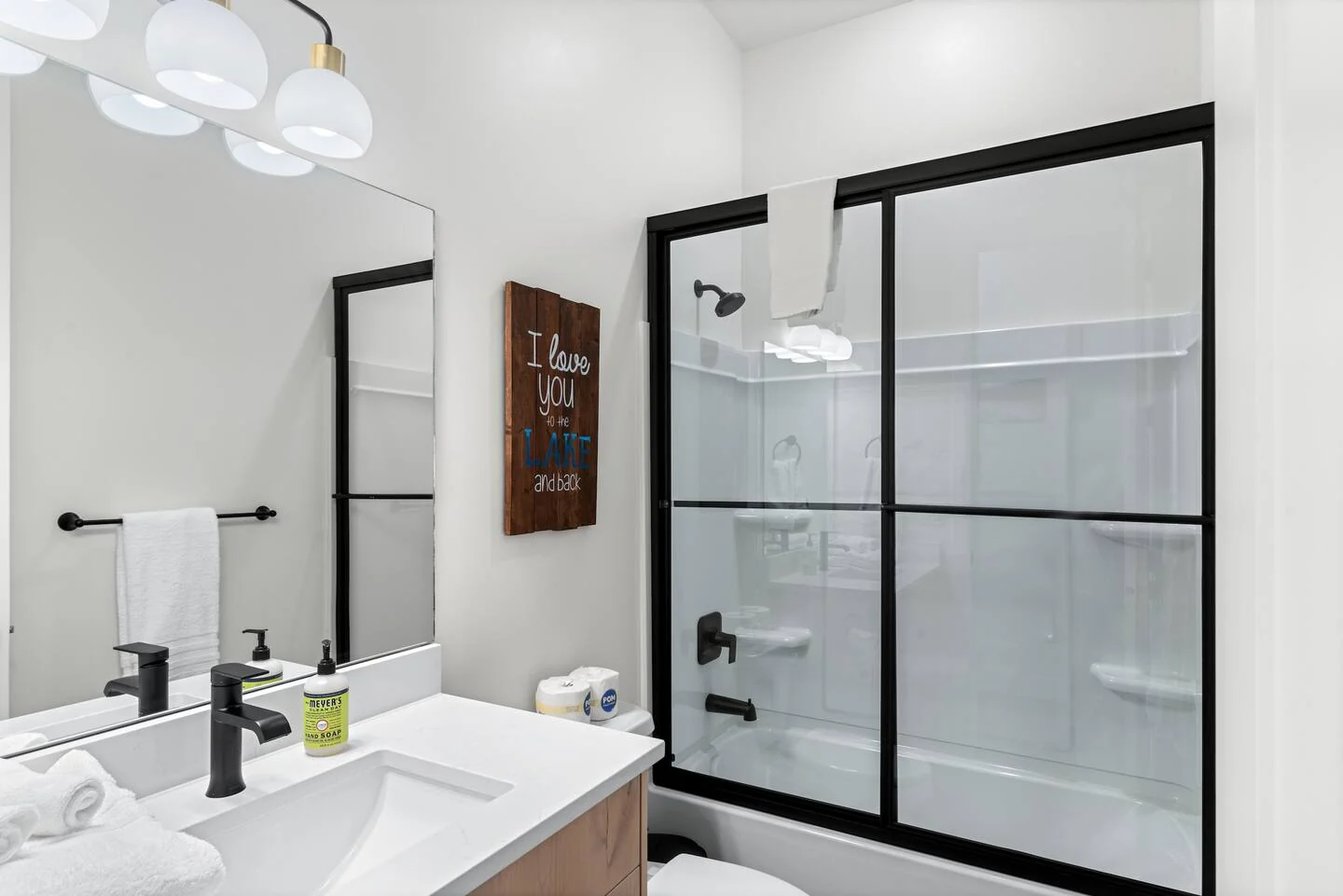 Bathroom with a wood-tone vanity, black-framed glass shower, black fixtures, white walls, and folded towels — Denali, Bear Lake.