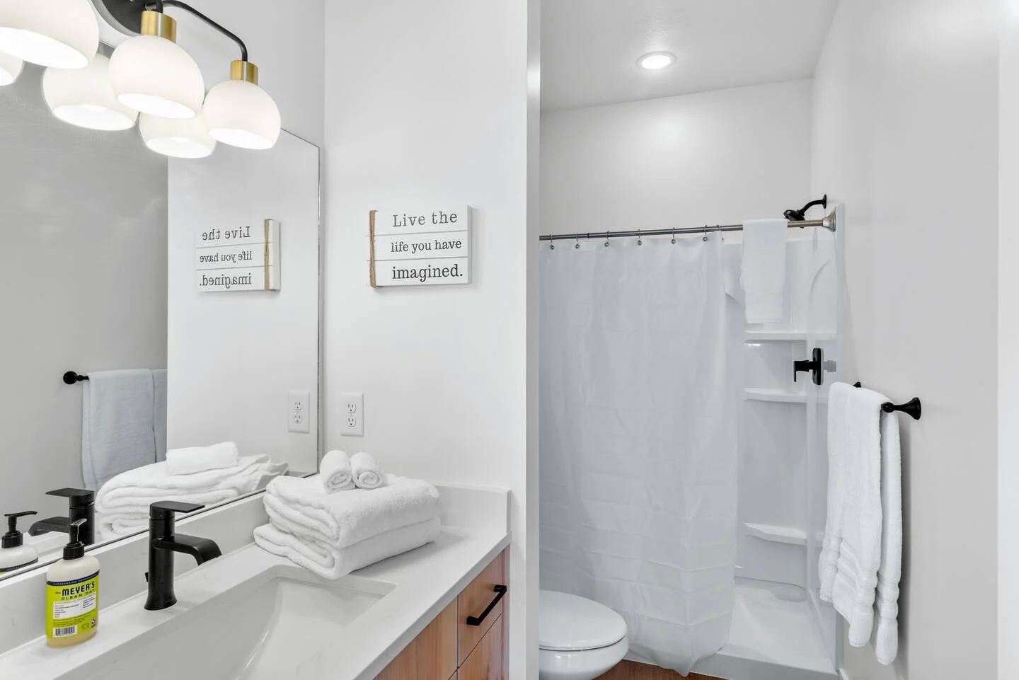 Bathroom with a single vanity, white shower surround, black fixtures, folded towels, and a toilet — Denali, Bear Lake.