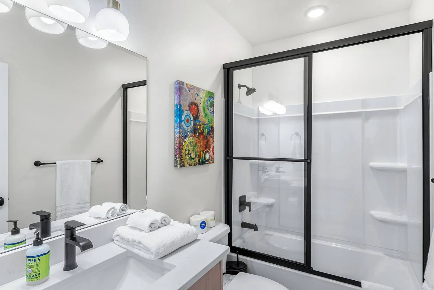 Bathroom featuring a single vanity, black-framed glass shower enclosure, white walls, and a colorful wall artwork — Denali, Bear Lake.