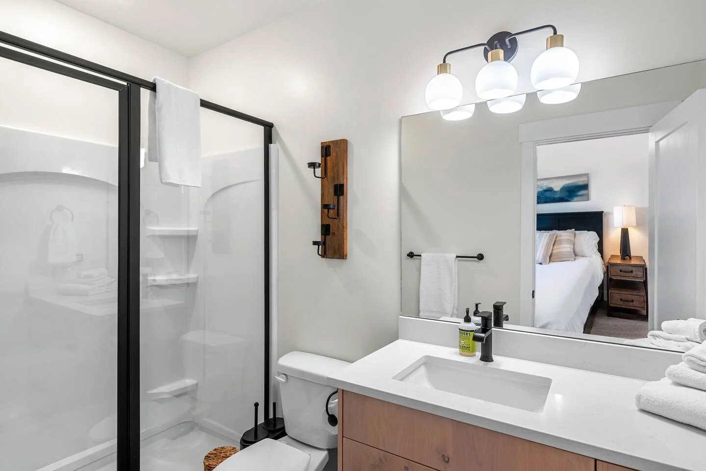 Bathroom with a black-framed shower, pale wood vanity, white countertop, black fixtures, and an open doorway — Denali, Bear Lake.