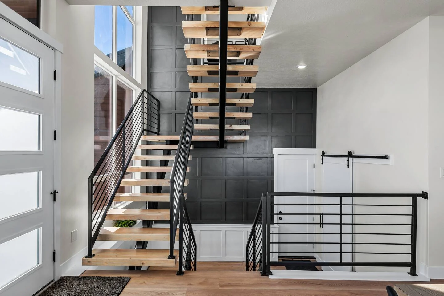 Entry hall with a floating wood staircase, black metal railings, white doors, and dark accent tile — Denali, Bear Lake.