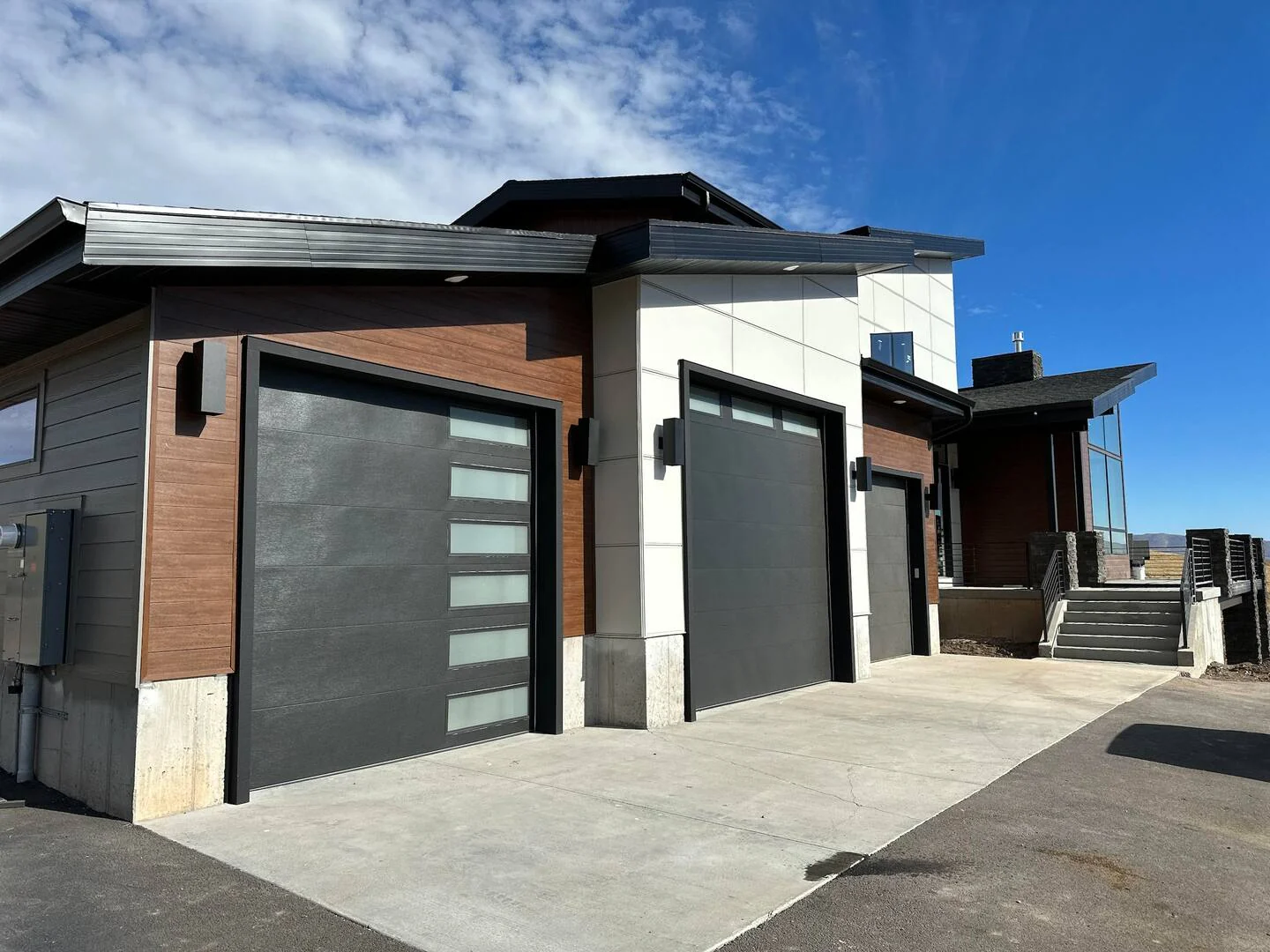 Contemporary exterior with multiple garage doors, wood-look cladding, concrete driveway, covered entry, and blue sky — Denali, Bear Lake.