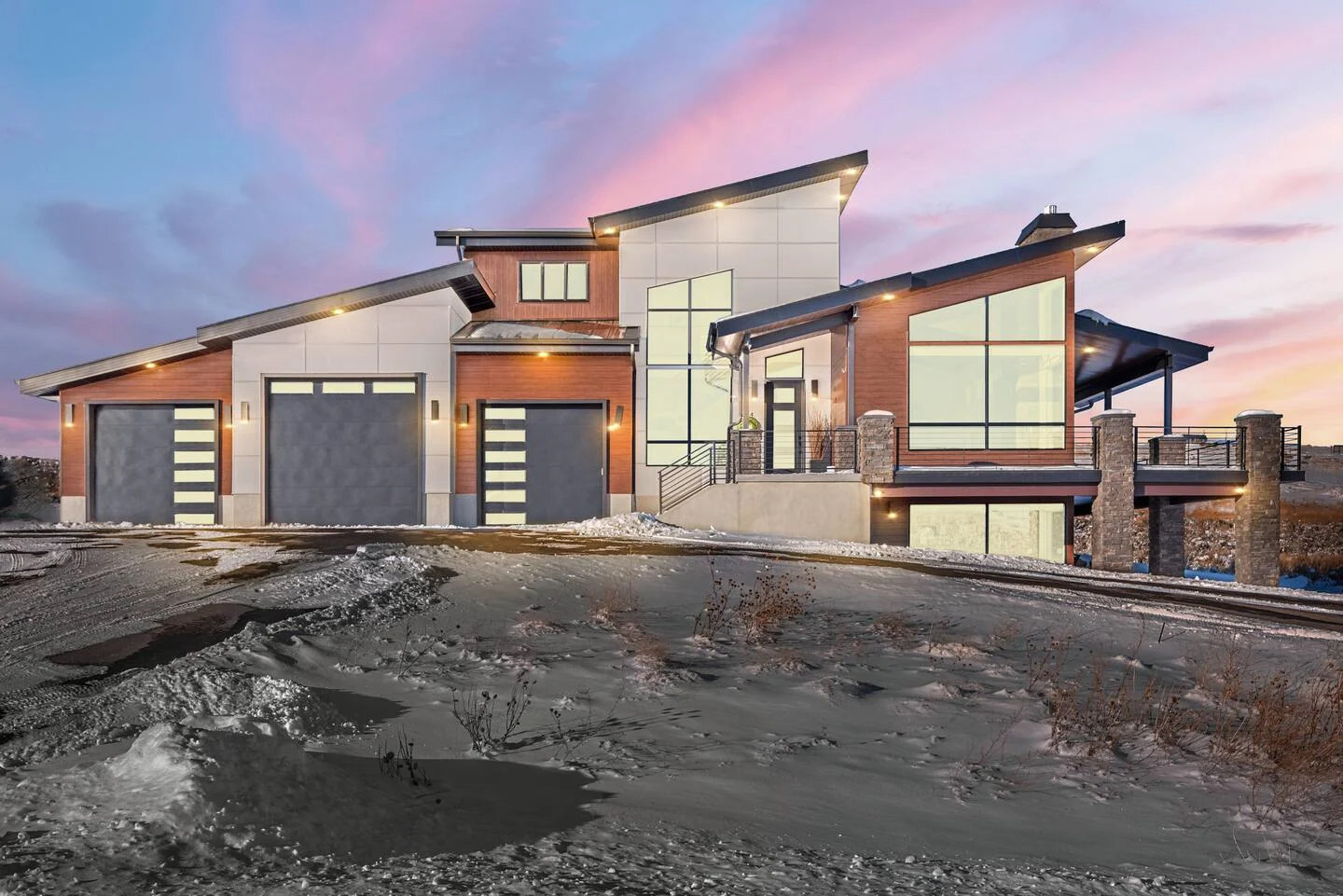 Front exterior view at dusk showing a contemporary facade, garage doors, illuminated windows, driveway, and cloudy sky — Denali, Bear Lake.