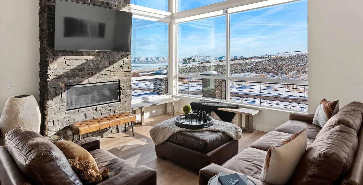 Living room with stone fireplace, mounted television, upholstered seating, round coffee table, and broad exterior-facing windows — Denali, Bear Lake.