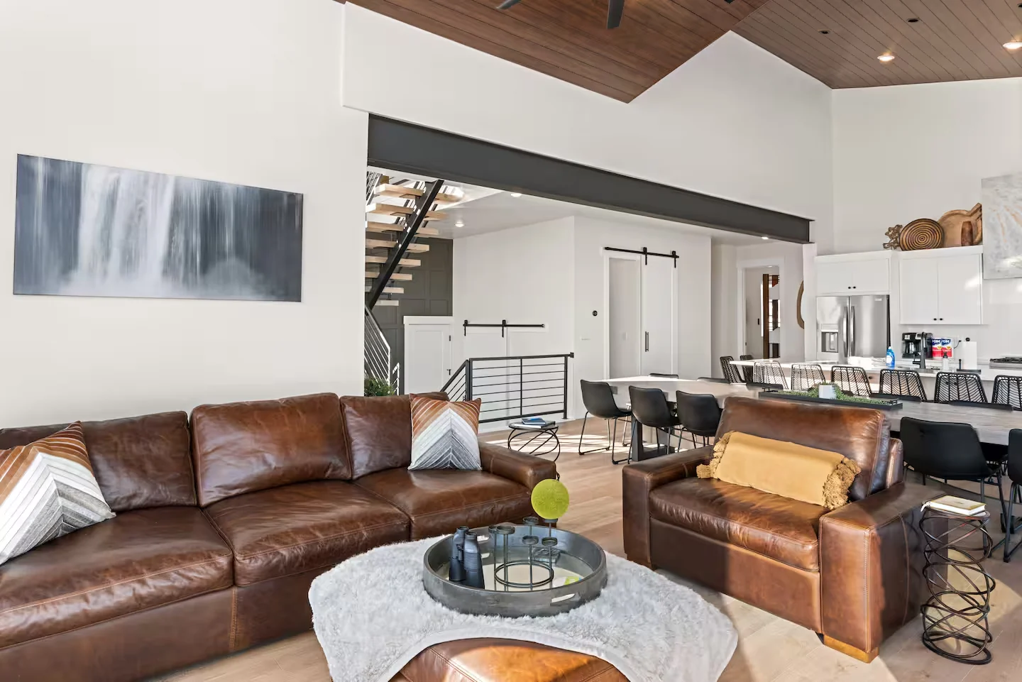 Main living area with leather seating, stone fireplace, coffee table, wood ceiling inset, and kitchen beyond — Denali, Bear Lake.