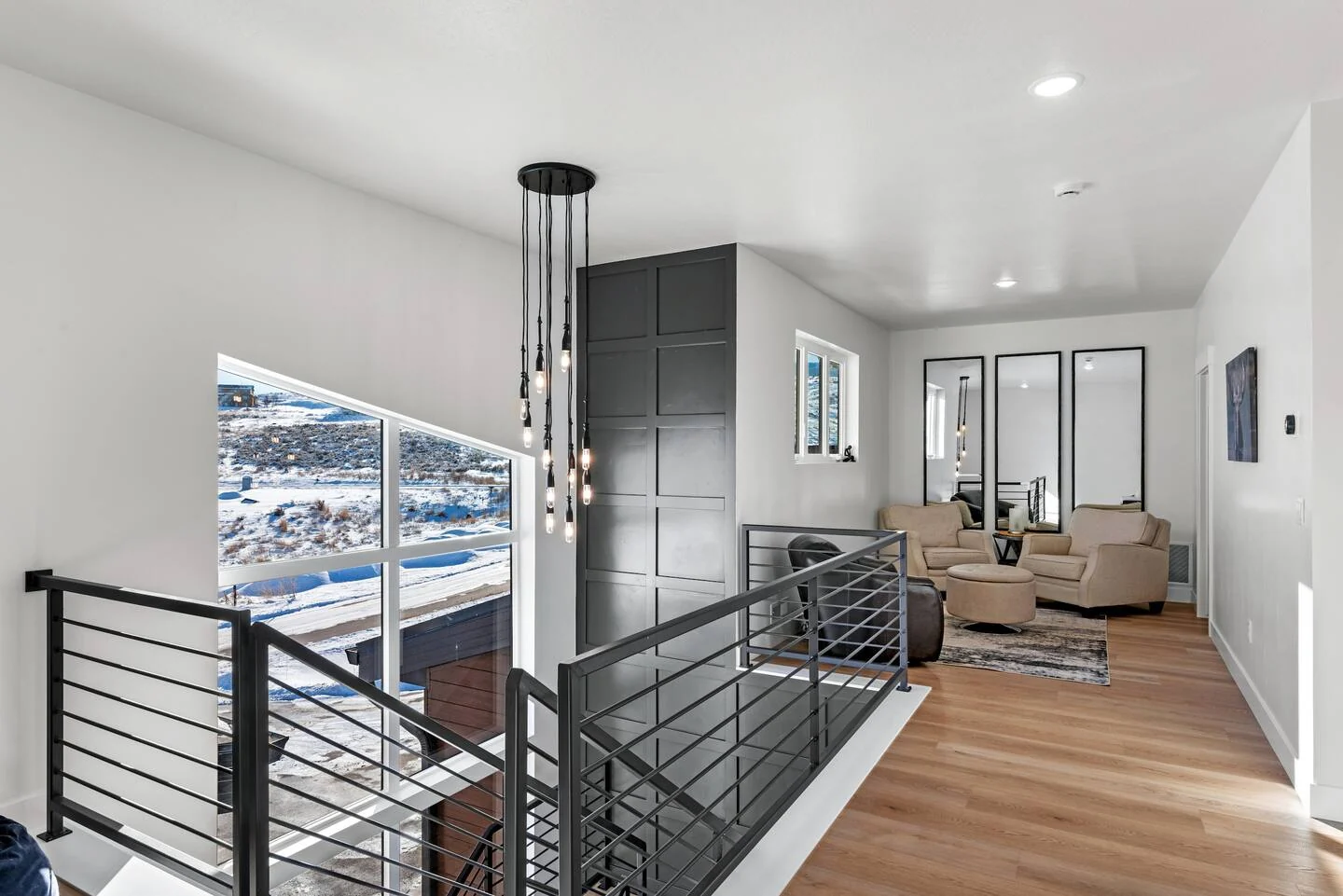 Loft landing with black metal railings, pale wood flooring, seating area, pendant lights, and tall windows — Denali, Bear Lake.