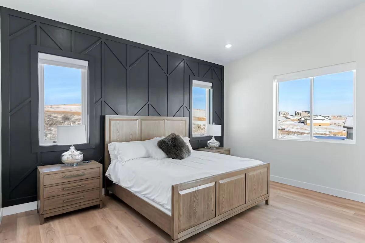 Main bedroom with wood bed frame, dark paneled accent wall, nightstands, hardwood-style flooring, and windows — Denali, Bear Lake.