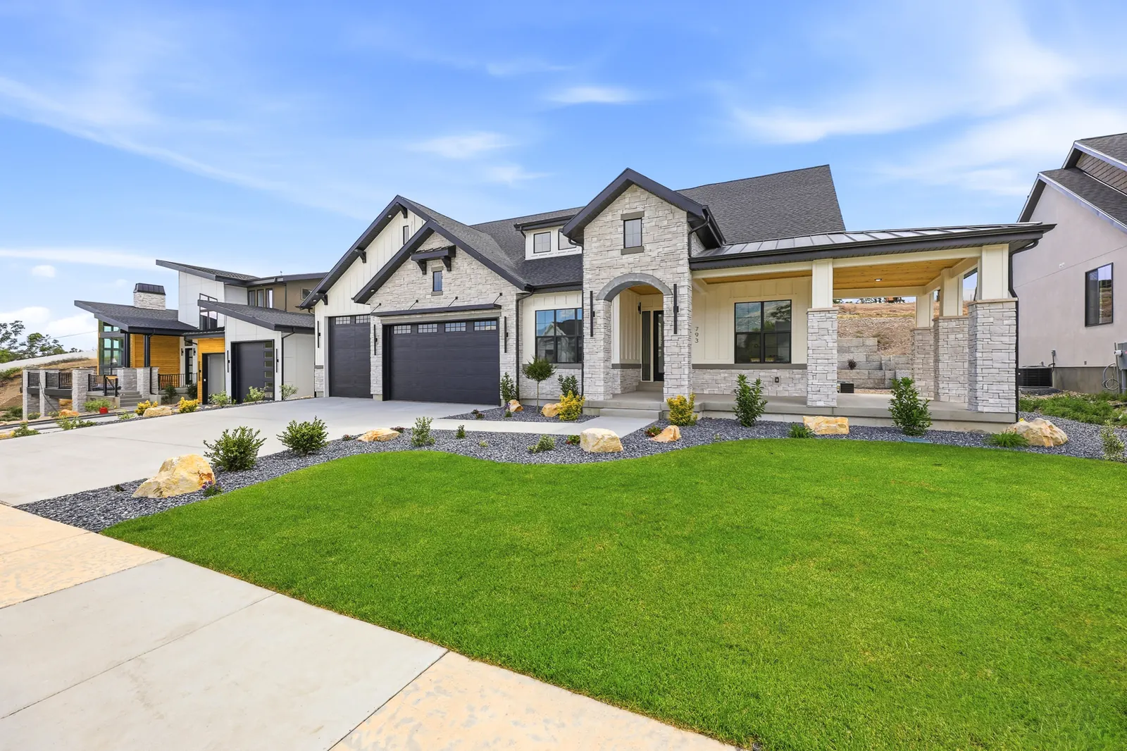 Front exterior with green lawn, stone-and-siding facade, dark garage doors, and fresh landscaping in Olympic BH08, American Fork.