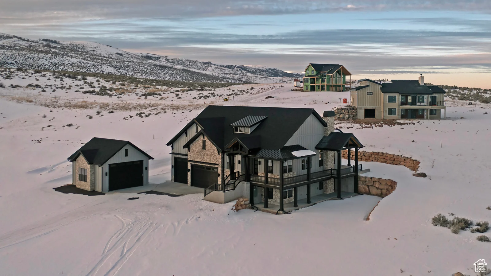 Aerial photo of a snow-covered home, detached garage, and neighboring homes beneath a cloudy sky — Olympic, Bear Lake.
