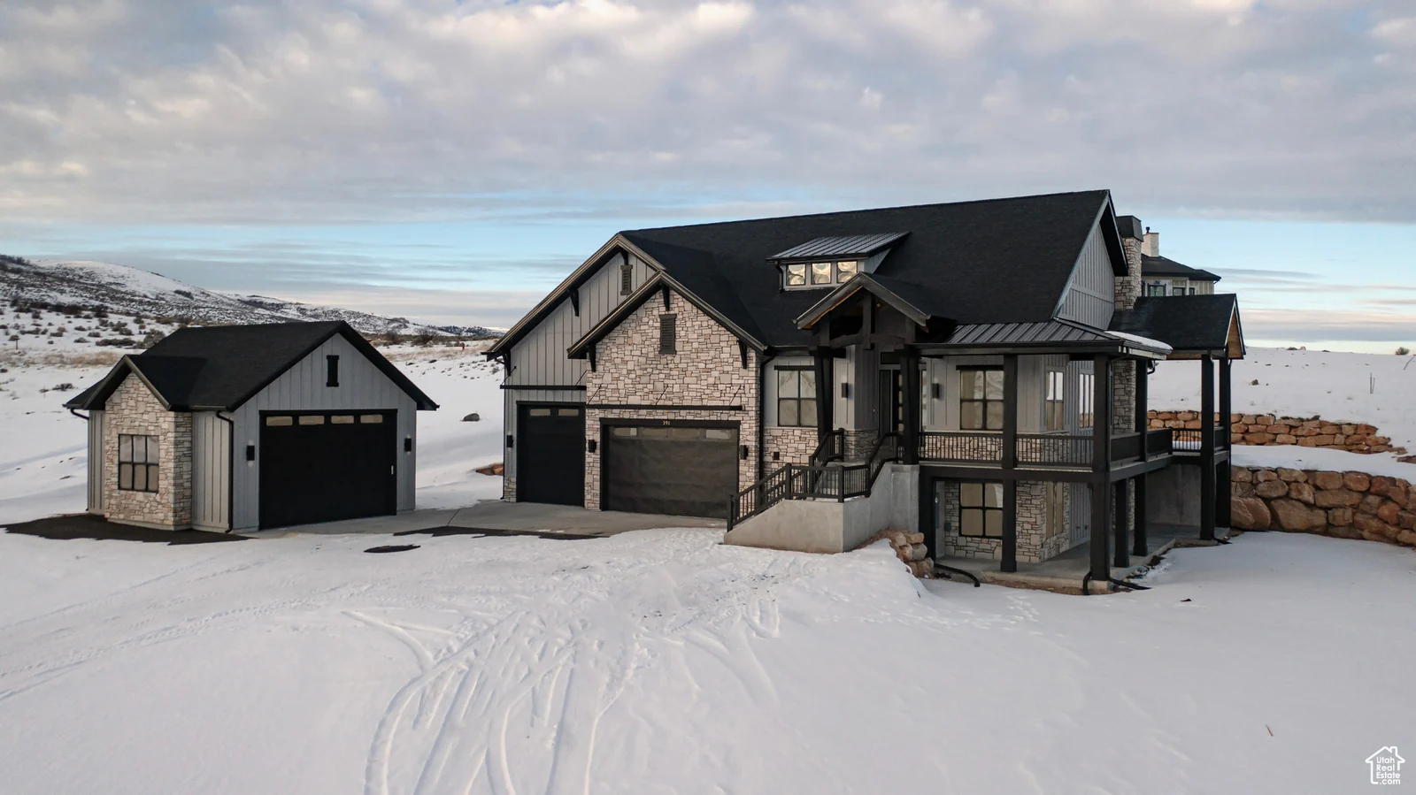 Front exterior photo showing stone accents, covered porch, attached garage, and detached garage in snowy surroundings — Olympic, Bear Lake.