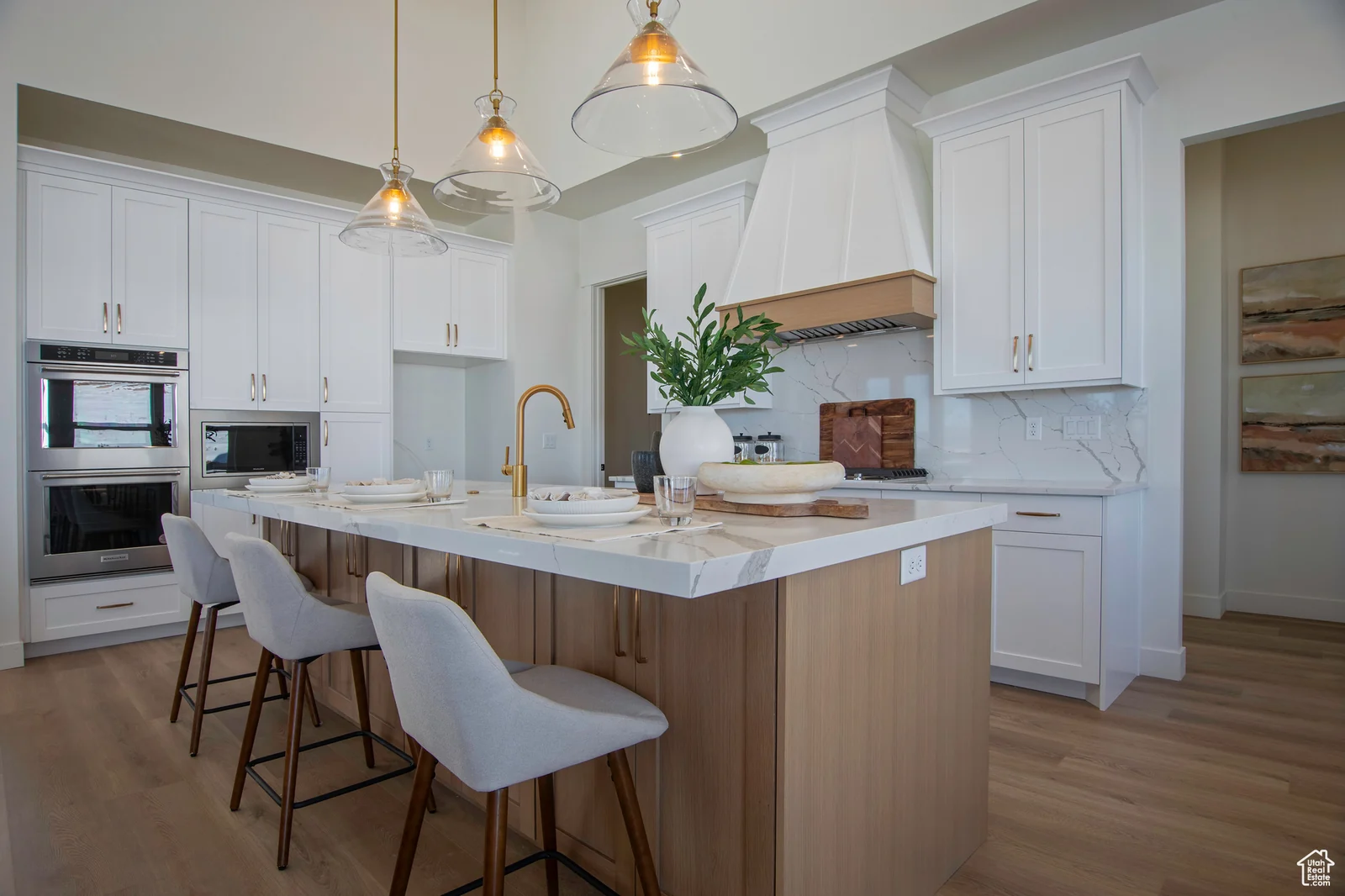 Kitchen photo featuring a large waterfall-edge island, bar stools, white cabinetry, pendant lights, double ovens, and range hood — Olympic, Bear Lake.