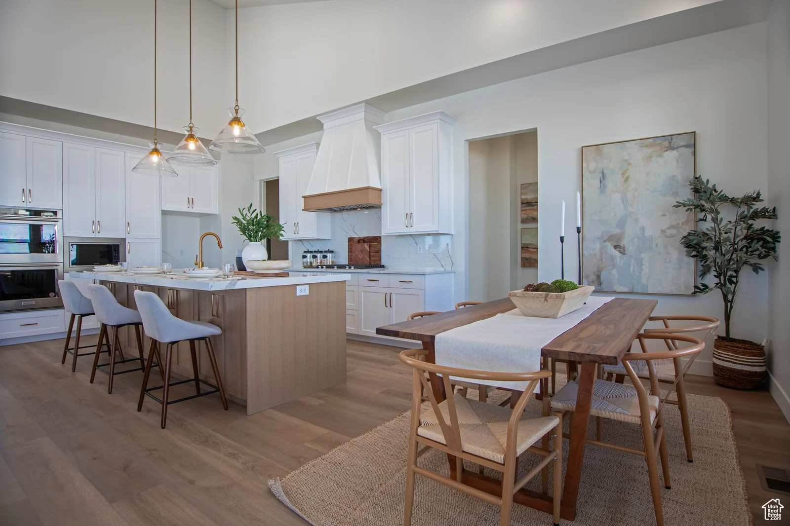 Kitchen and dining area with a wood table, white cabinetry, island seating, pendant lights, and range hood — Olympic, Bear Lake.