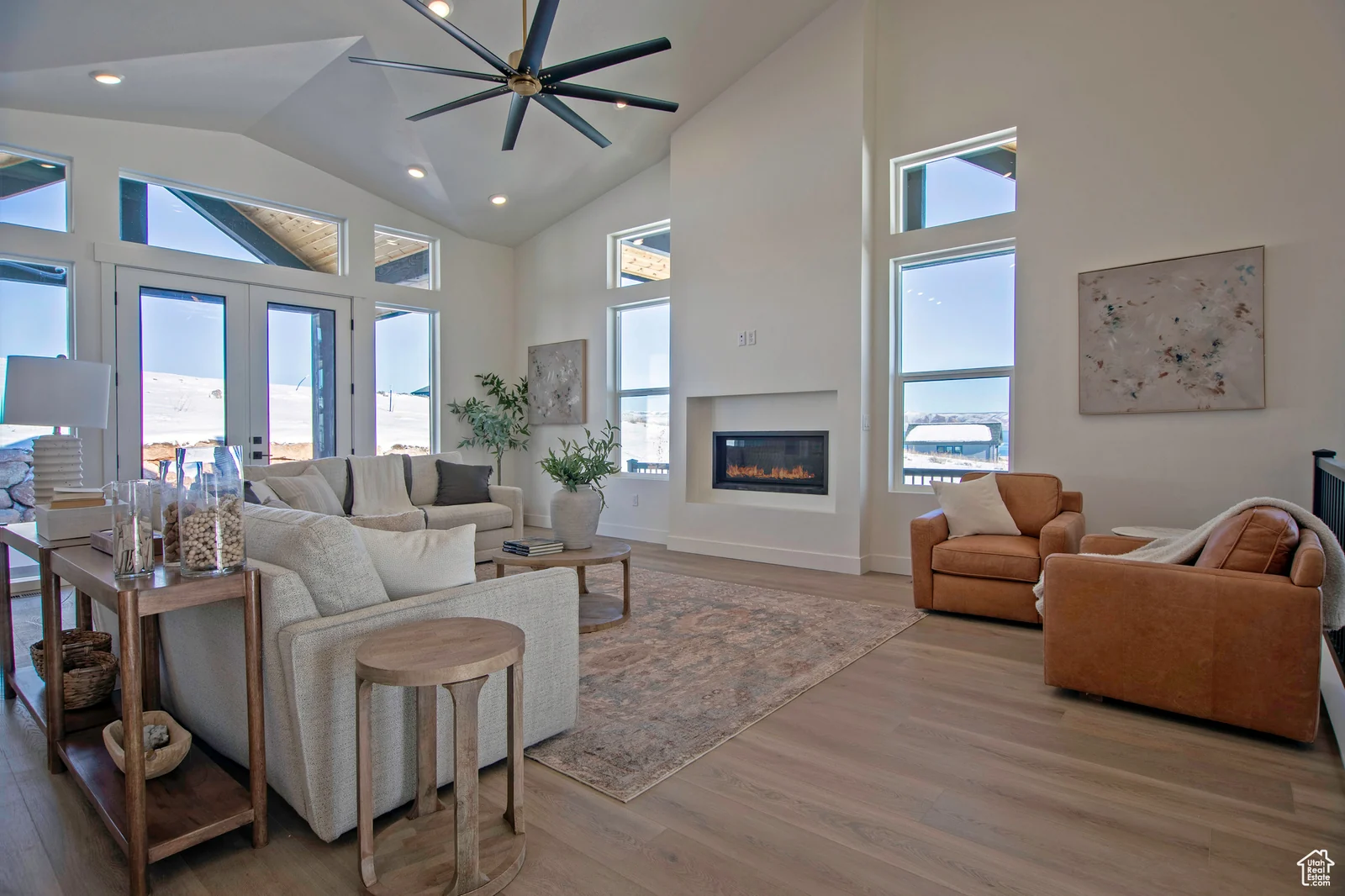Living room with tall windows, glass doors, fireplace, ceiling fan, seating, and views of the snow-covered surroundings — Olympic, Bear Lake.