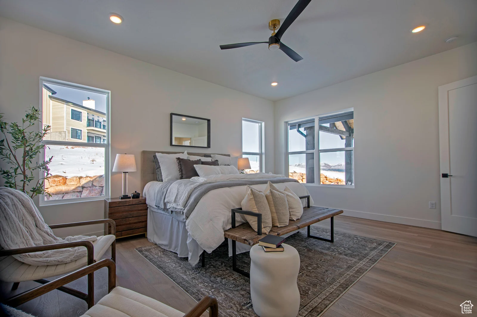 Primary bedroom photo with a large bed, bench, armchair, ceiling fan, bedside tables, and windows overlooking snow — Olympic, Bear Lake.