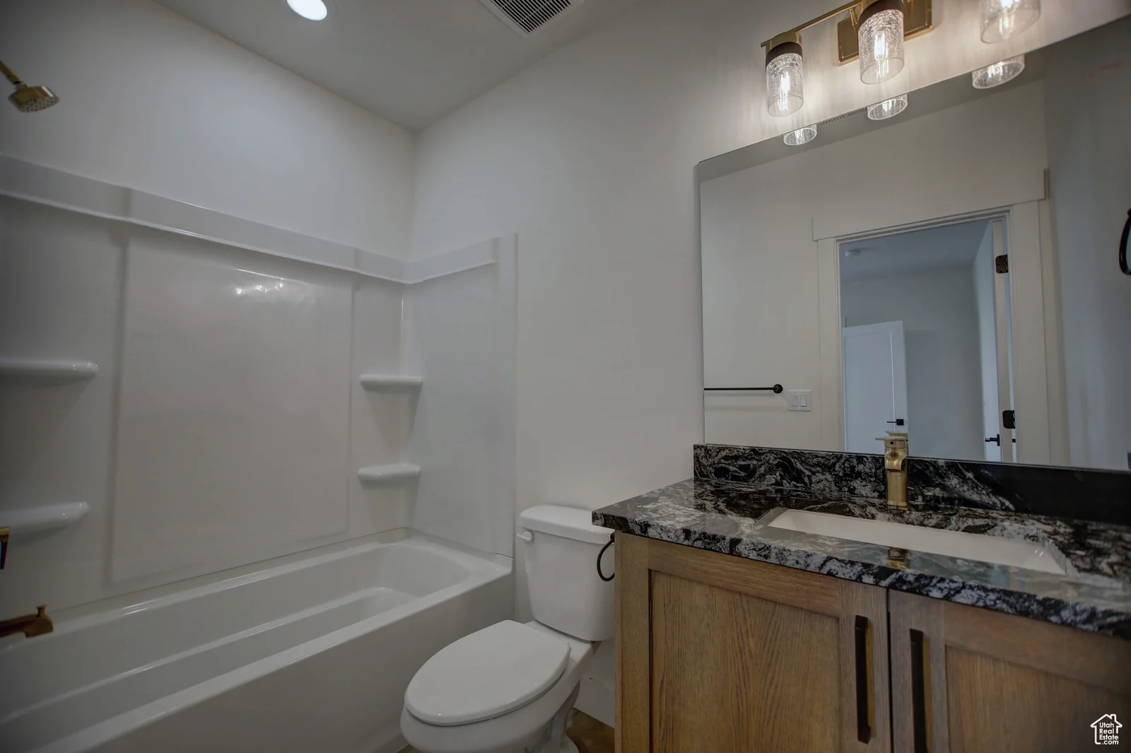 Basement bathroom with single wood vanity, stone-look counter, toilet, mirror, and wall shelving in Pinnacle, Bear Lake.