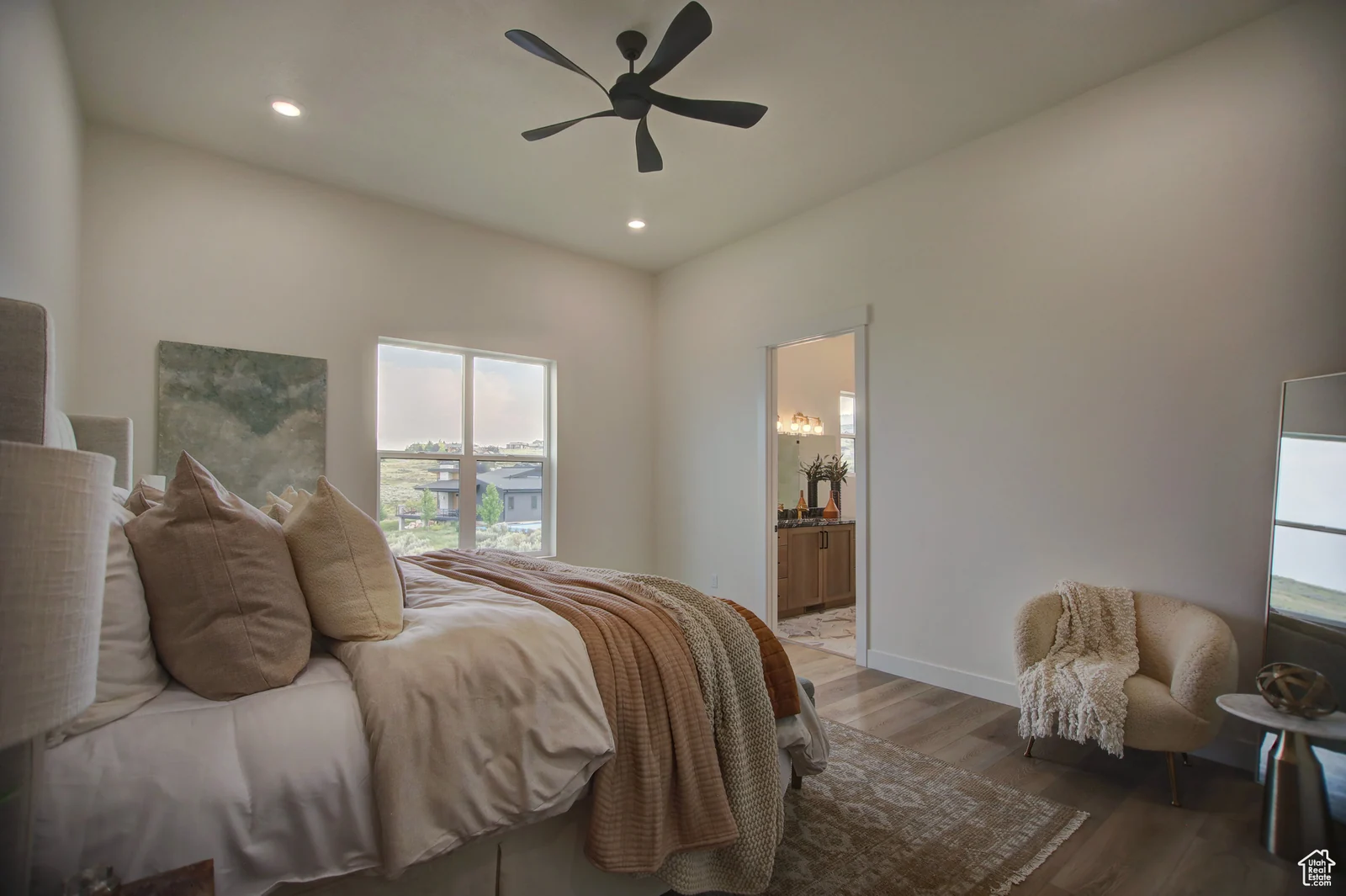 Staged bedroom with a bed, ceiling fan, wood-look flooring, and windows facing open land in Pinnacle, Bear Lake.