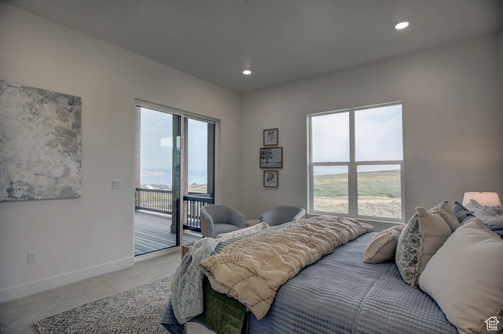 Staged bedroom with a made bed, upholstered chair, wall art, and windows overlooking open land in Pinnacle, Bear Lake.