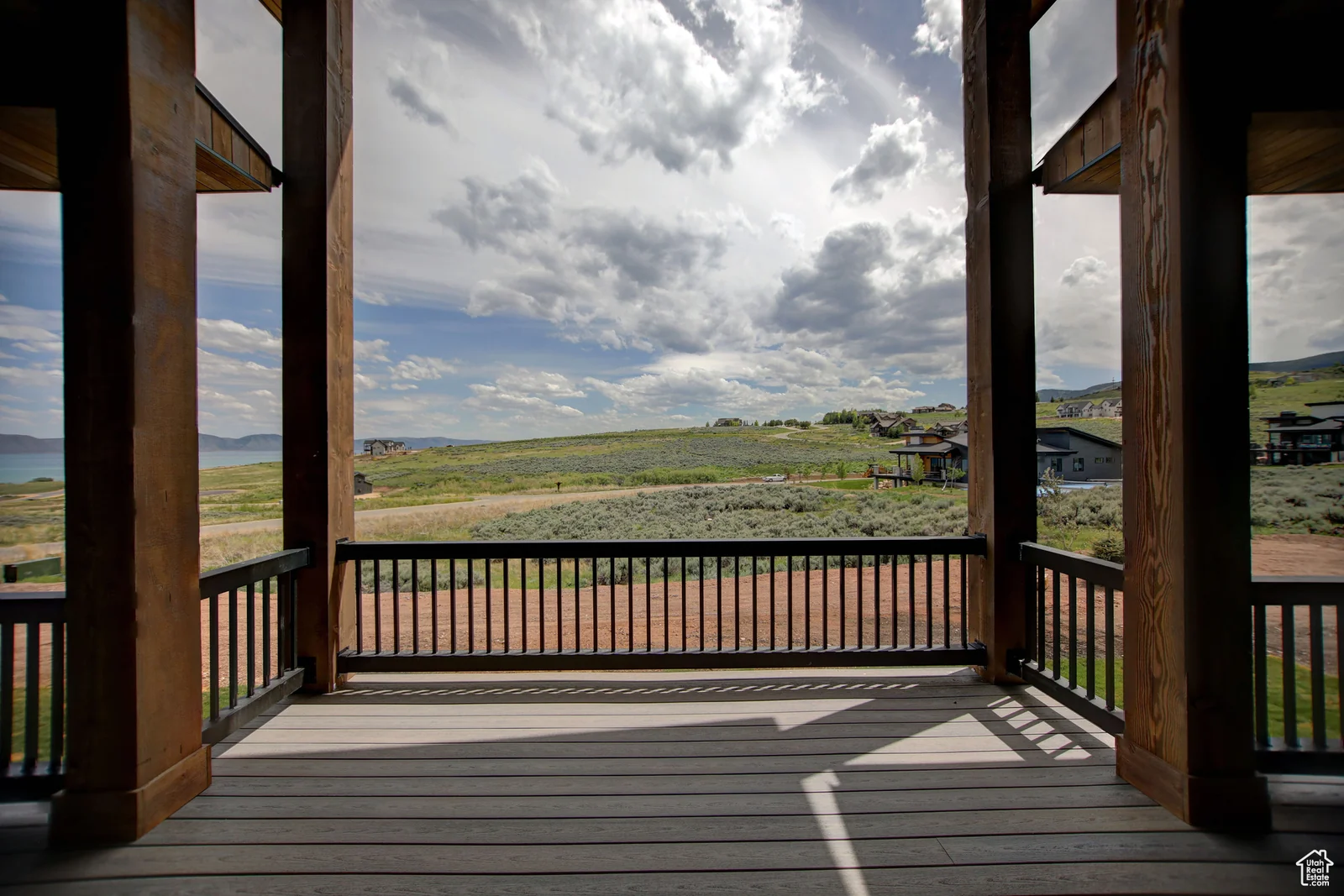 View from the covered wood deck through dark posts and railing toward rolling open terrain in Pinnacle, Bear Lake.