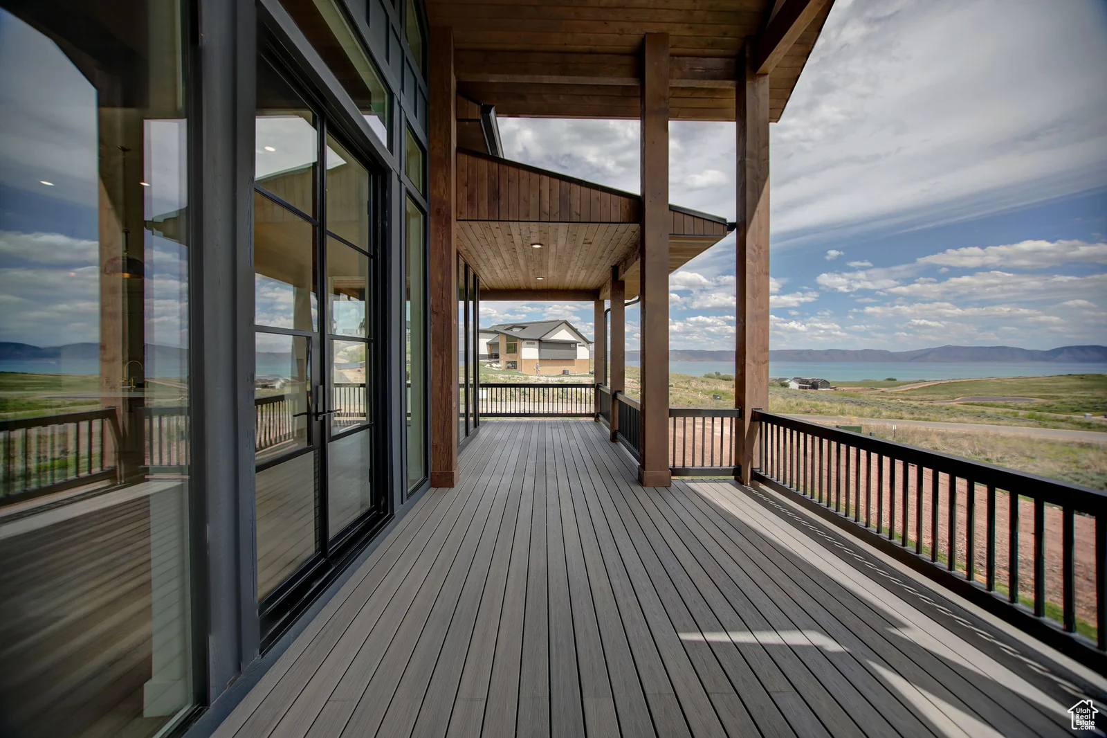Covered wood deck alongside the home with railing, posts, and views across surrounding open land in Pinnacle, Bear Lake.