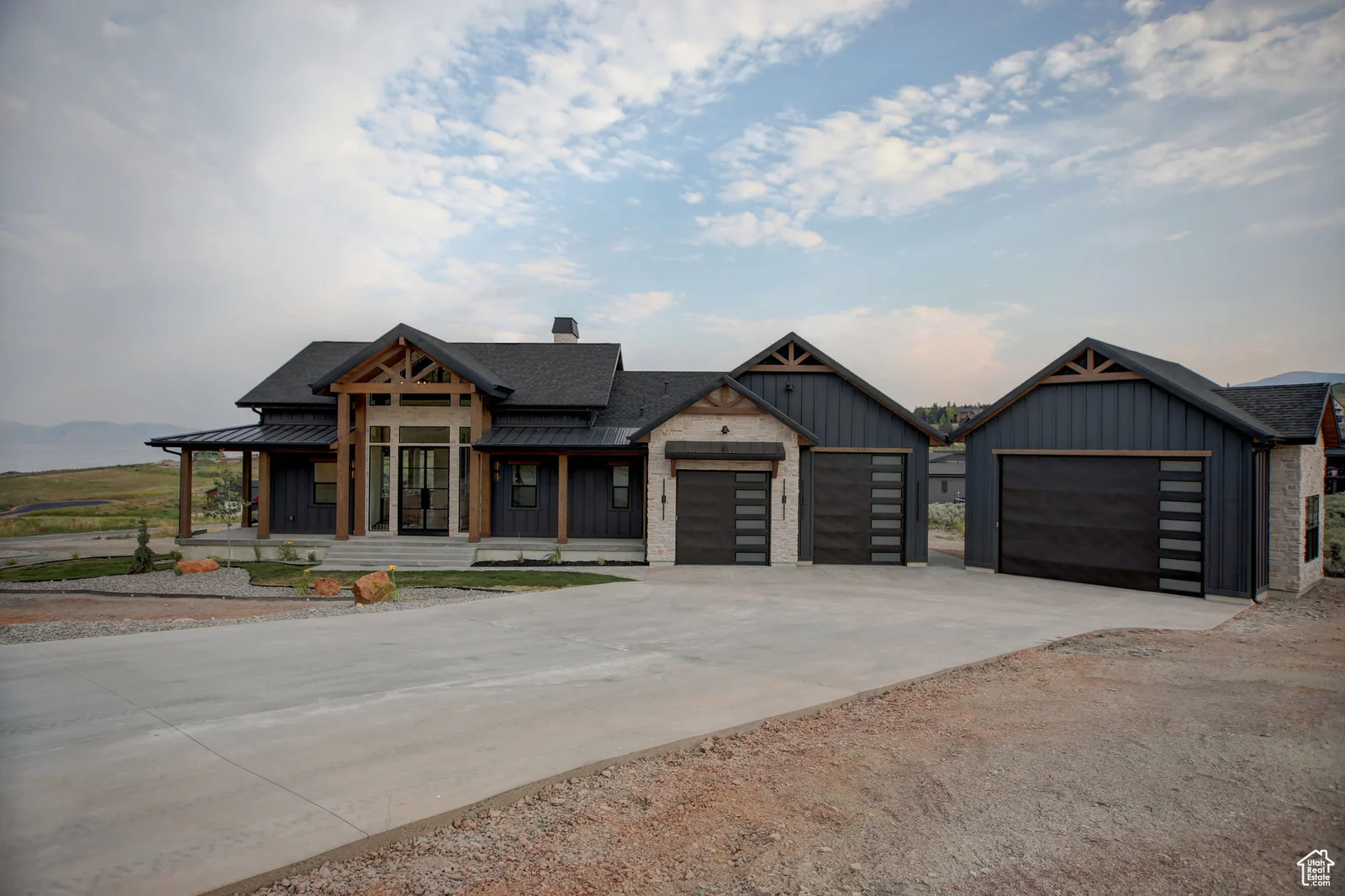 Front view of dark-sided home with covered entry, three garage doors, driveway, and sparse landscaping in Pinnacle, Bear Lake.