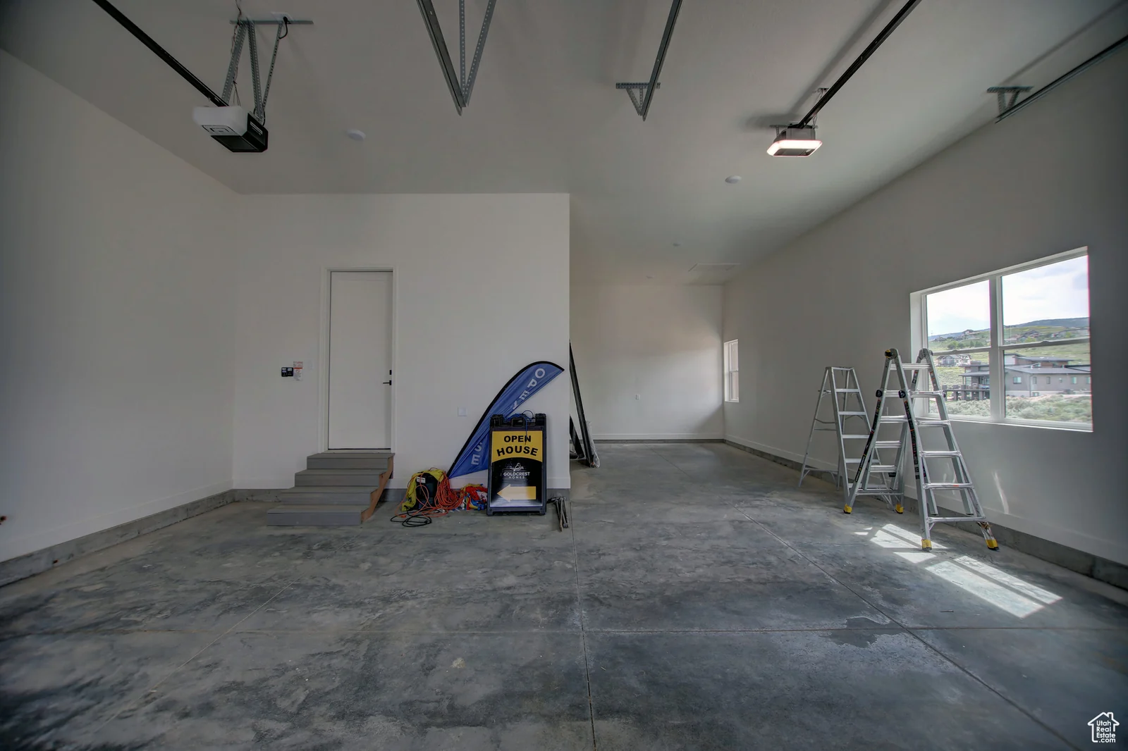 Garage interior with concrete floor, wall-mounted garage door, windows, storage items, and a short stairway in Pinnacle, Bear Lake.