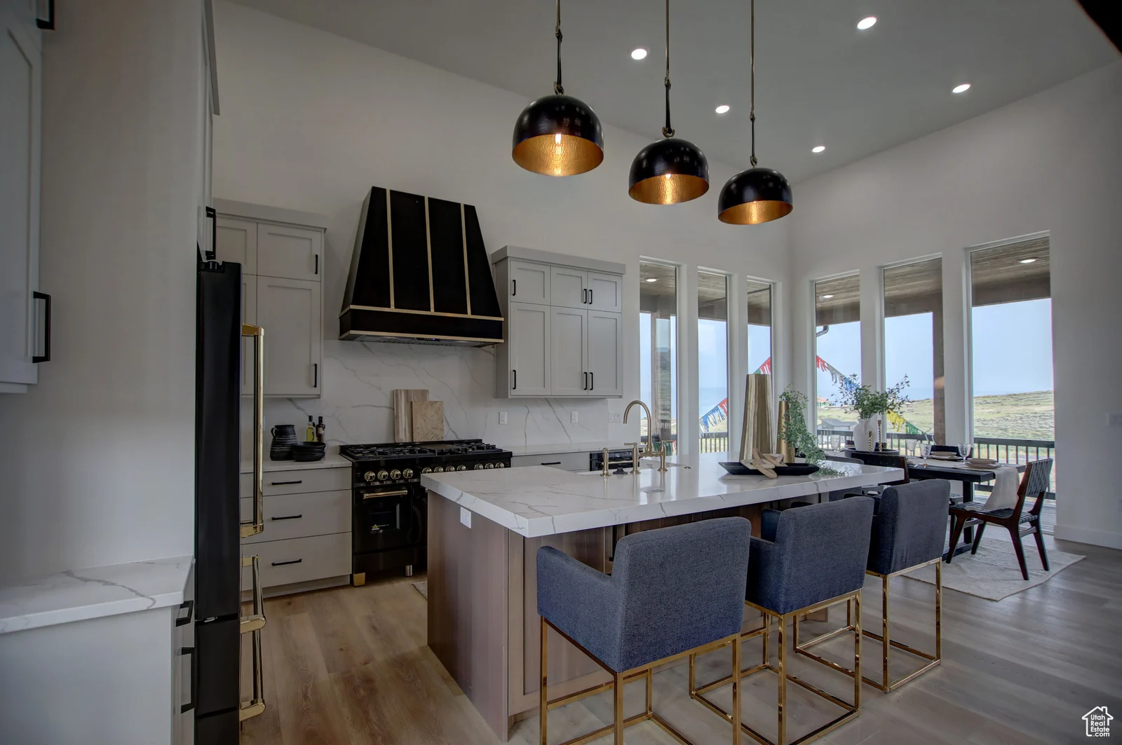 Kitchen with white cabinetry, island seating, black pendant lights, stainless appliances, and windows around the dining space in Pinnacle, Bear Lake.