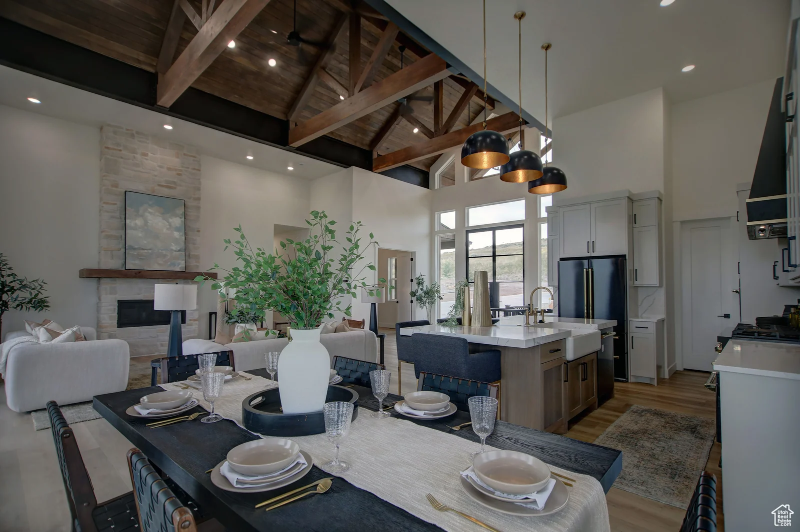 Open dining and living area with a set table, vaulted wood trusses, stone fireplace, and kitchen in Pinnacle, Bear Lake.