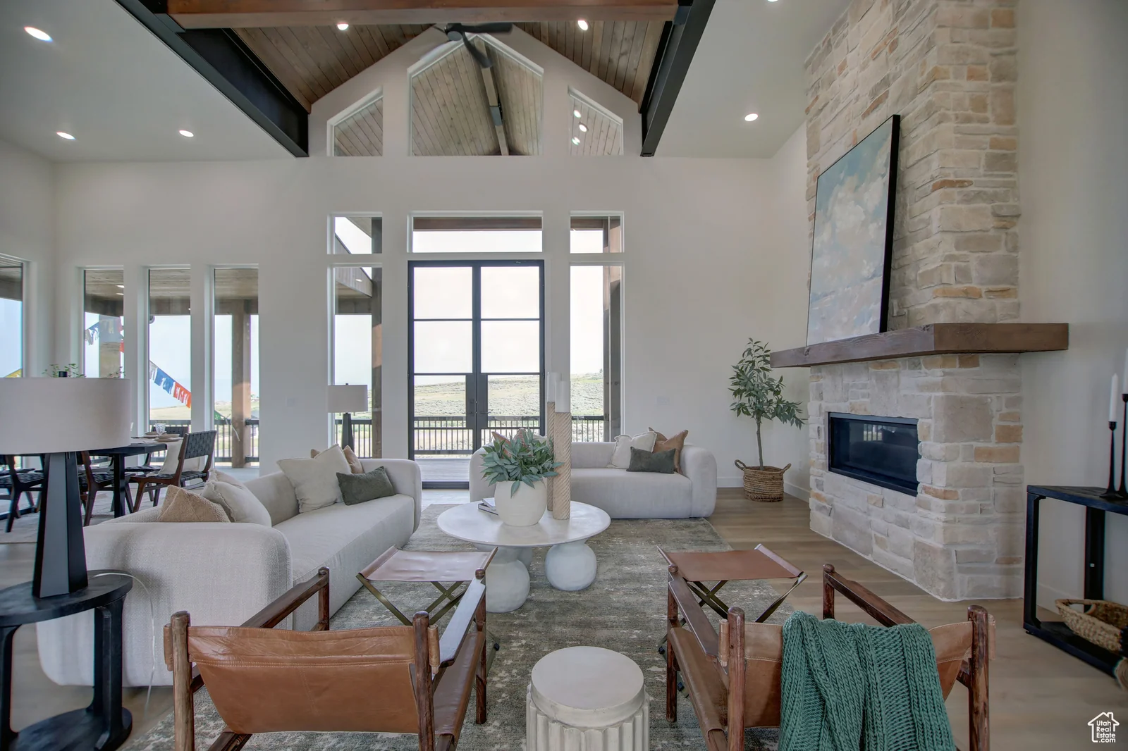 Vaulted great room with exposed wood trusses, stone fireplace, seating area, dining table, and glass entry doors in Pinnacle, Bear Lake.