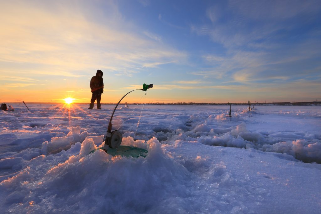winter landscape fishermen catch fish on a frozen river at sunset